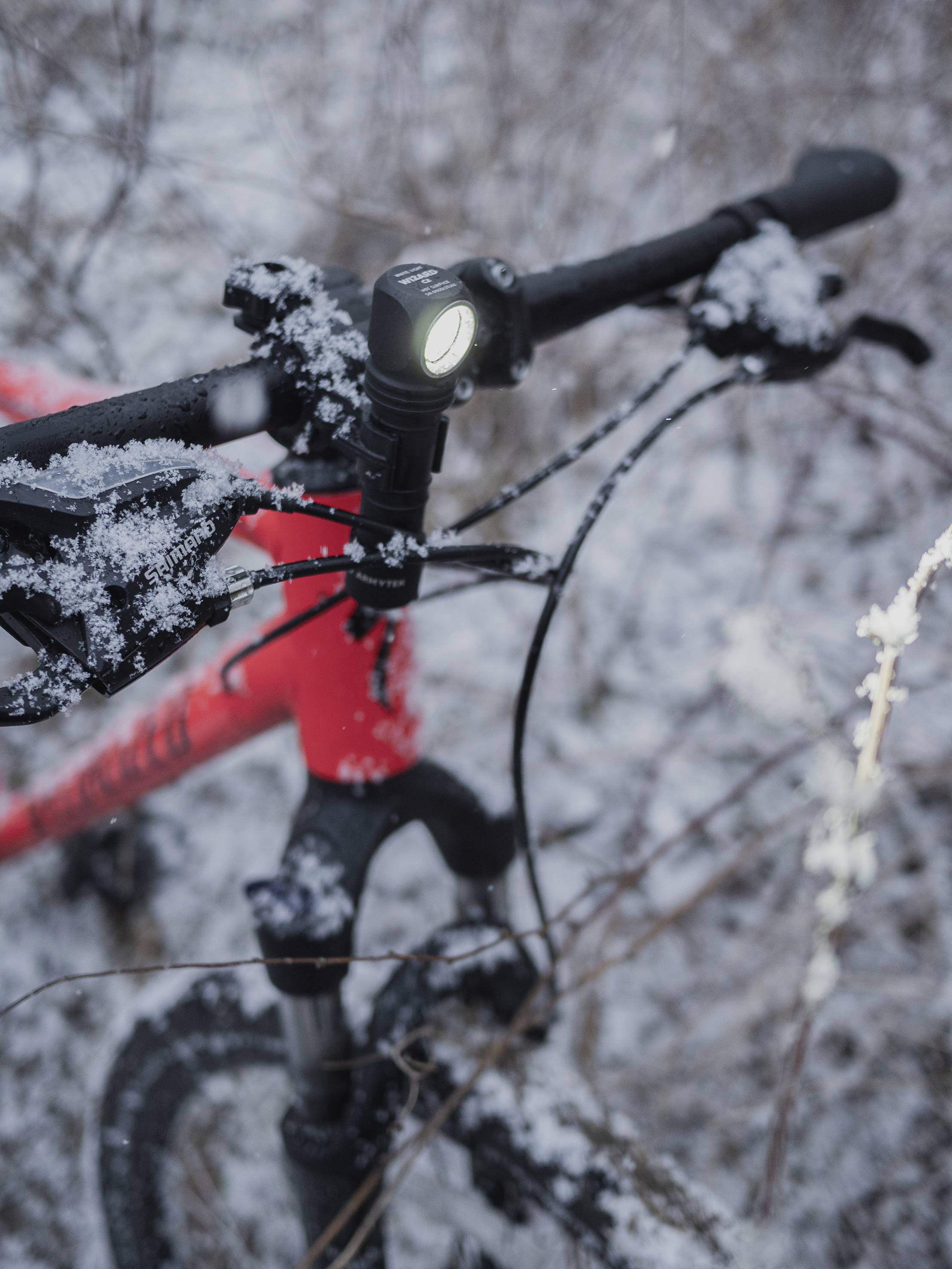 Rotes Fahrrad im Schnee, Vorderlicht eingeschaltet. Fahrräderlenker und -rahmen sind mit Schnee bedeckt. Winterliche Outdoor-Szene.