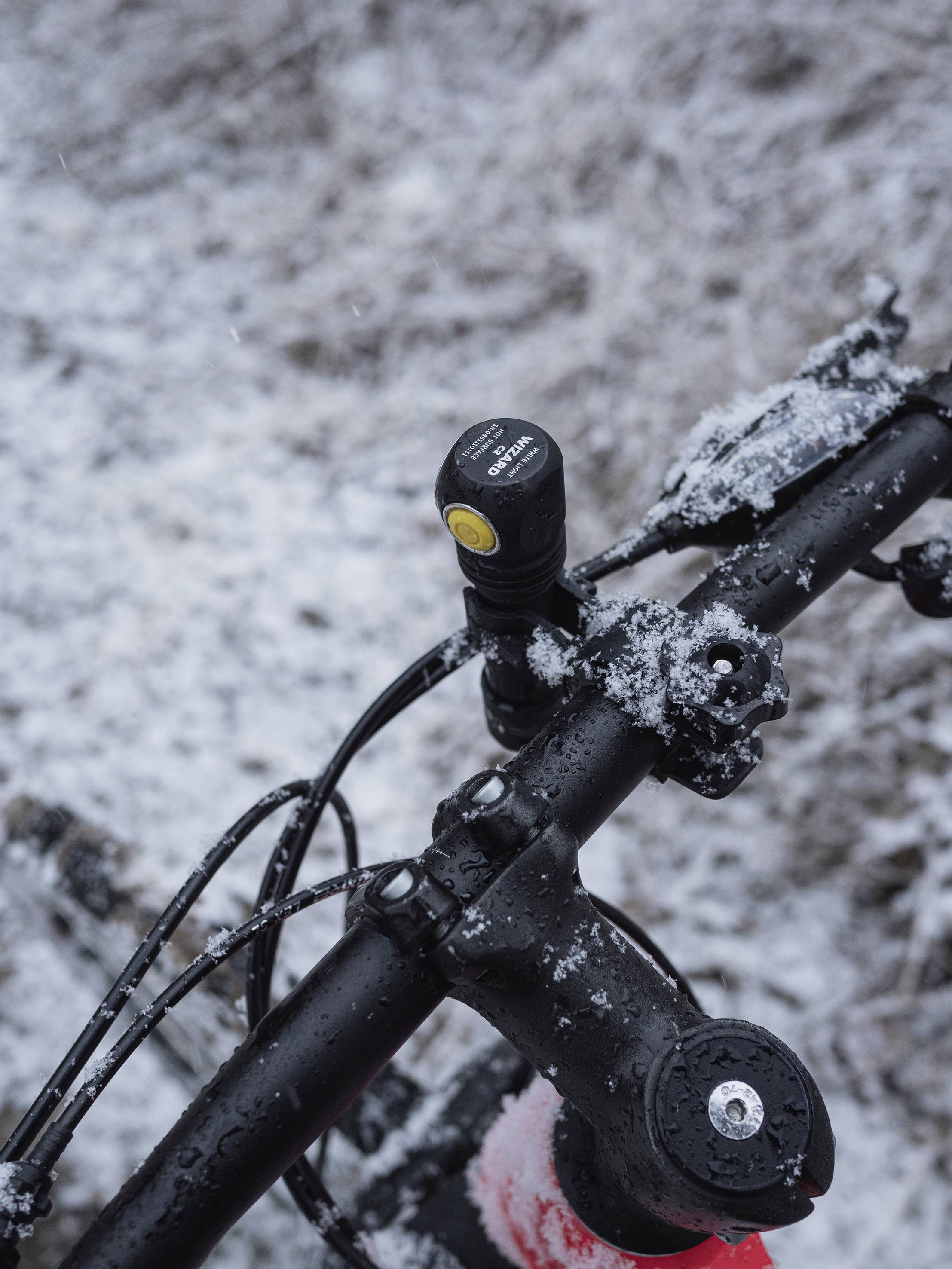 Ein Fahrradlenker mit Schnee bedeckt. Eine kleine Lampe ist darauf montiert. Im Hintergrund ist leicht Schnee zu sehen.
