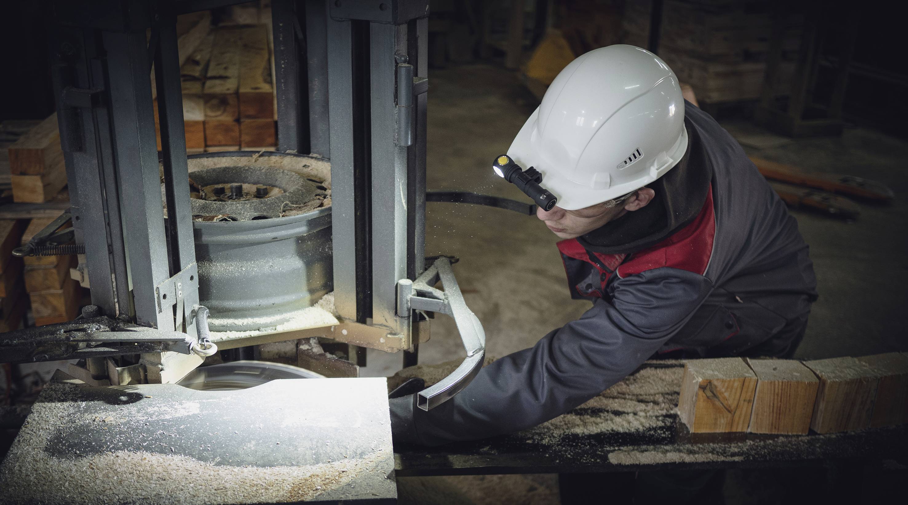 Arbeiter in Schutzkleidung bedient eine Holzbearbeitungsmaschine in einer Werkstatt. Späne und Holzstücke sind auf dem Tisch sichtbar.