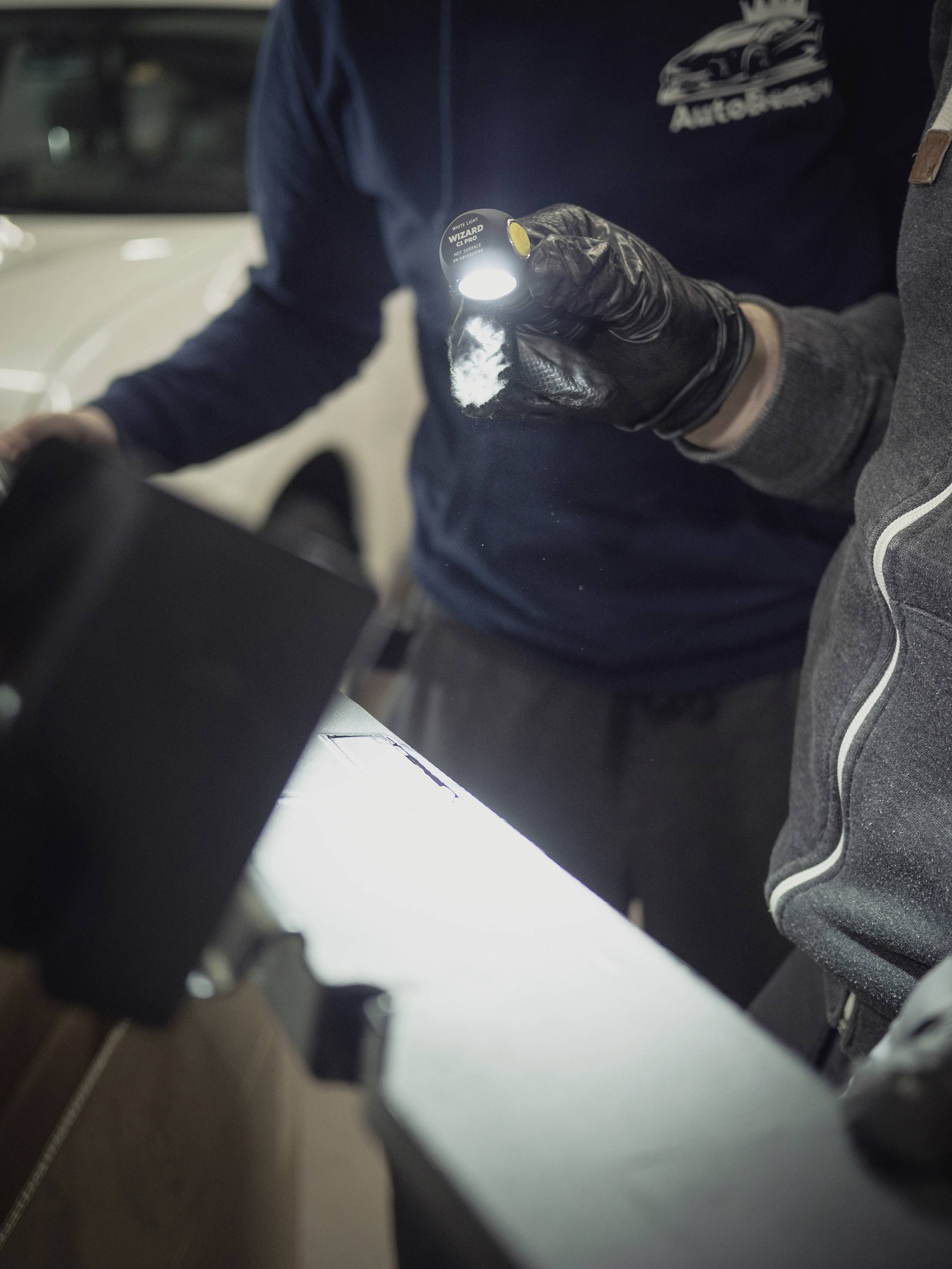 Zwei Personen inspizieren mit einer Taschenlampe ein Auto. Eine Person hält die Lampe, während die andere das Fahrzeug untersucht.