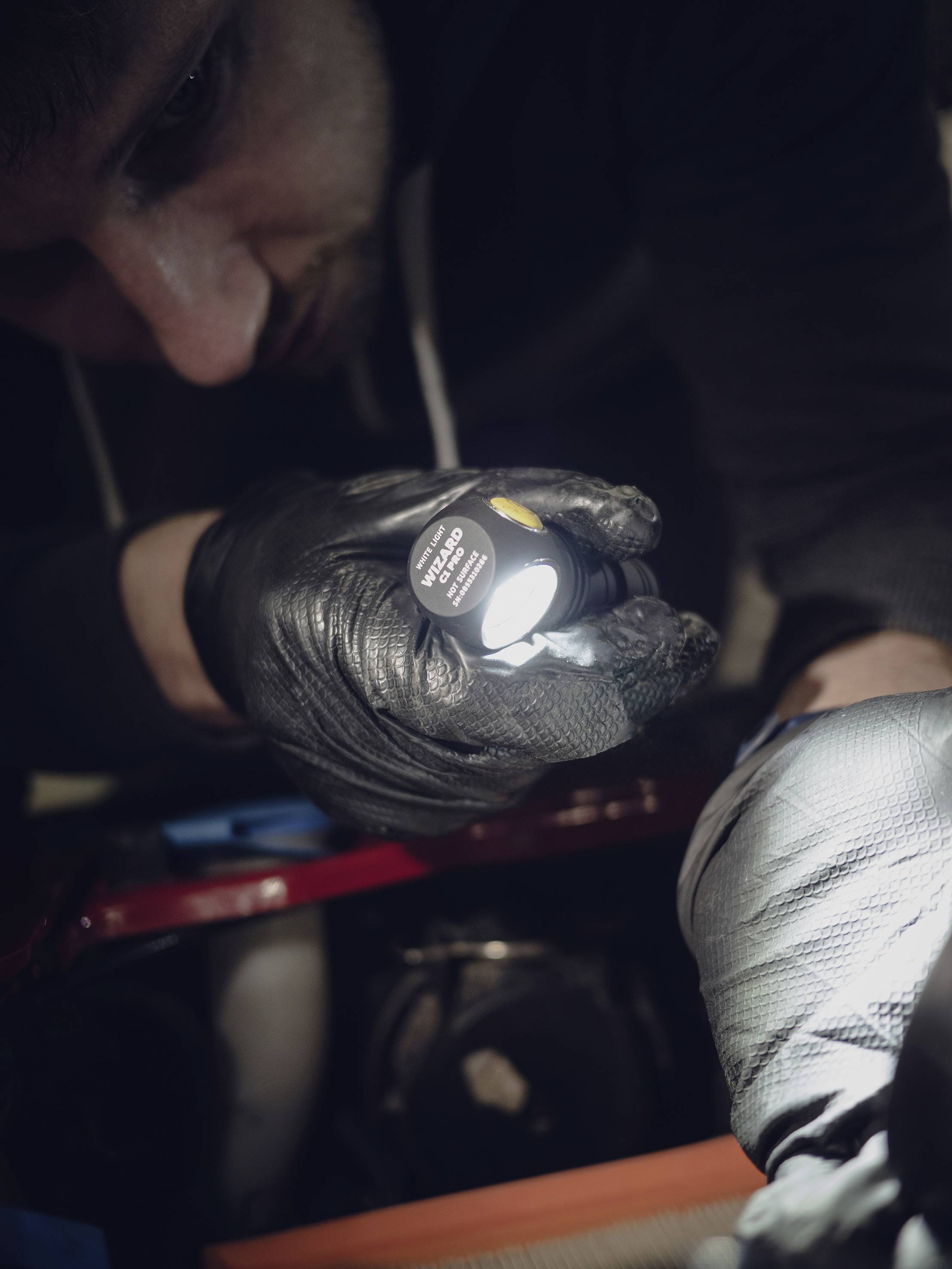 Ein Mensch untersucht mit einer Taschenlampe und trägt schwarze Handschuhe. Die Szene deutet auf manuelle Arbeit oder eine Inspektion hin.
