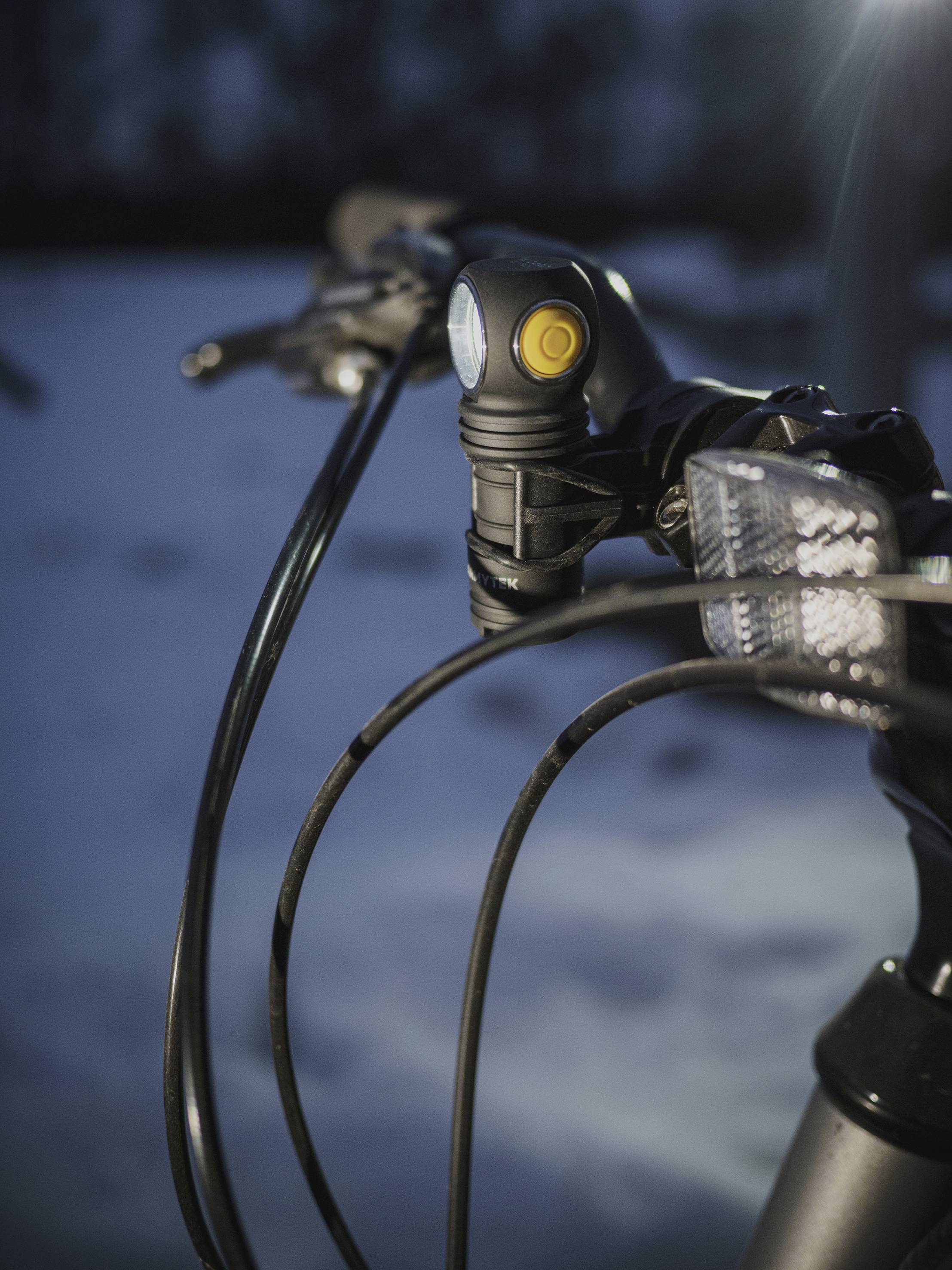 Ein Fahrradlenker im Fokus mit einem Frontlicht, Hintergrund dunkel und unscharf, möglicherweise in der Abenddämmerung aufgenommen.