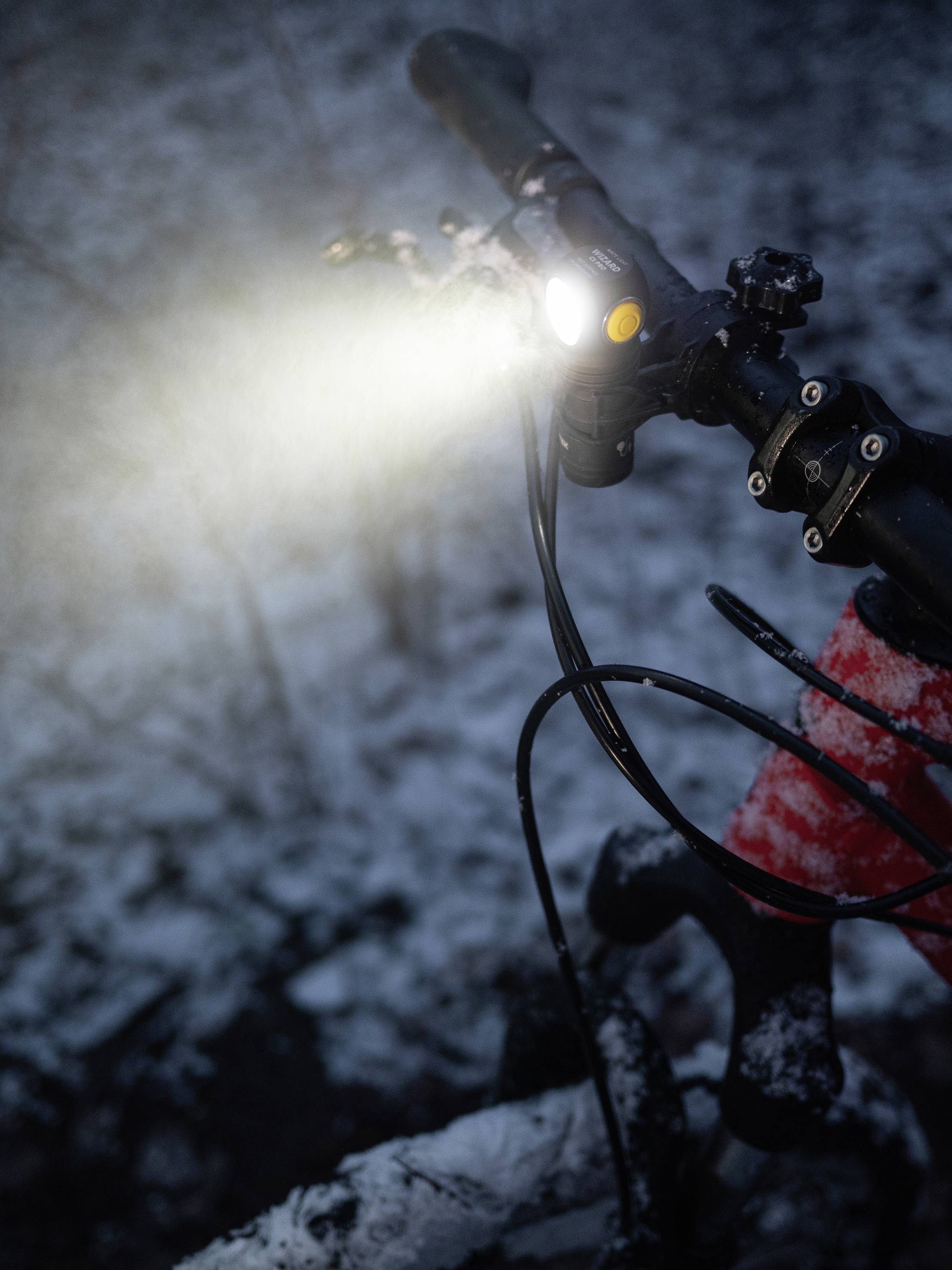 Fahrradlenker mit hell eingeschaltetem Licht, montiert in einer verschneiten Umgebung, symbolisiert Fahrt bei schlechten Sichtverhältnissen.