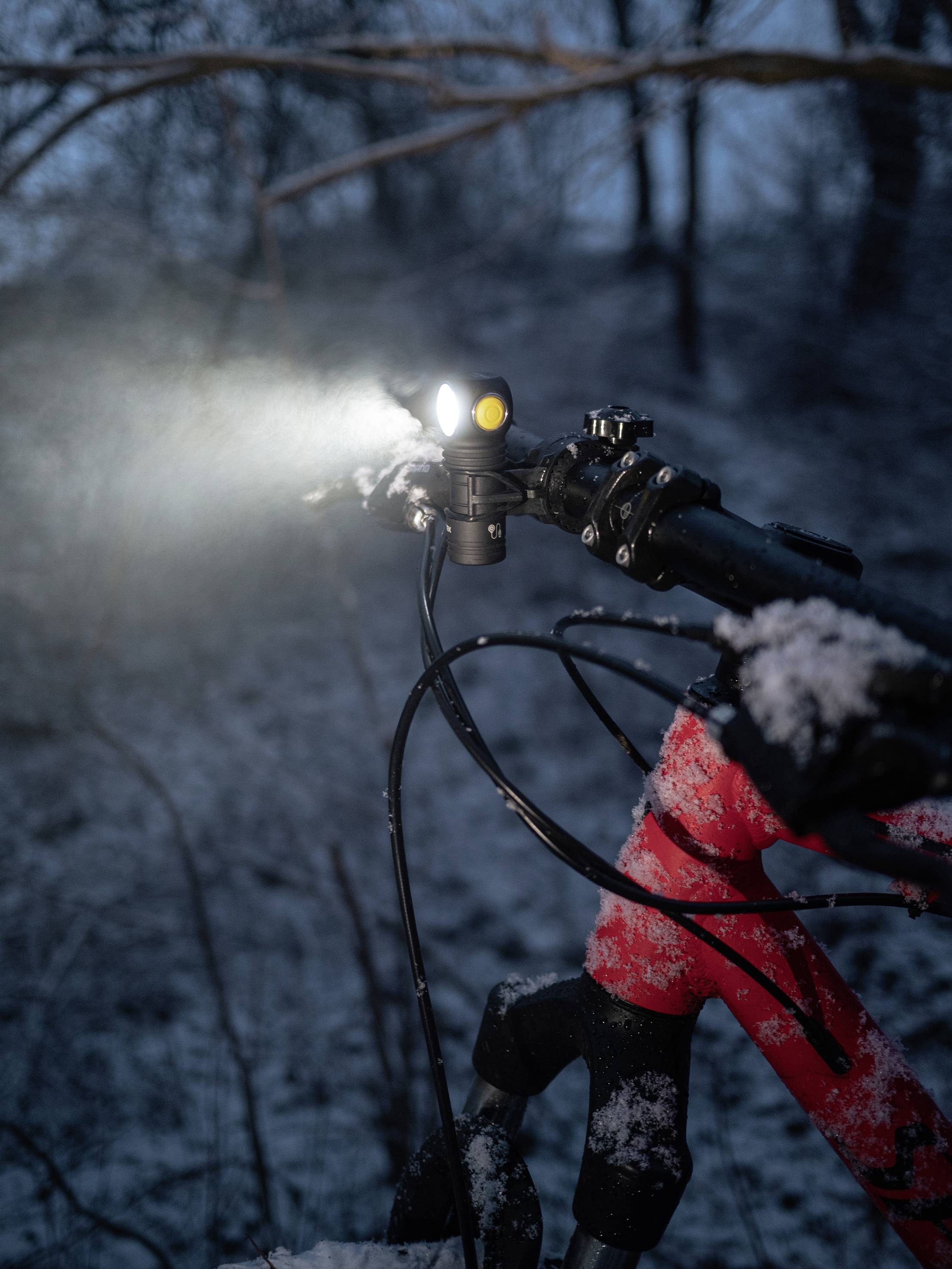 Ein rotes Fahrrad steht im Schnee, der Vorderlauf ist mit einer leuchtenden Lampe ausgestattet, die den Weg im Dunkeln erhellt.