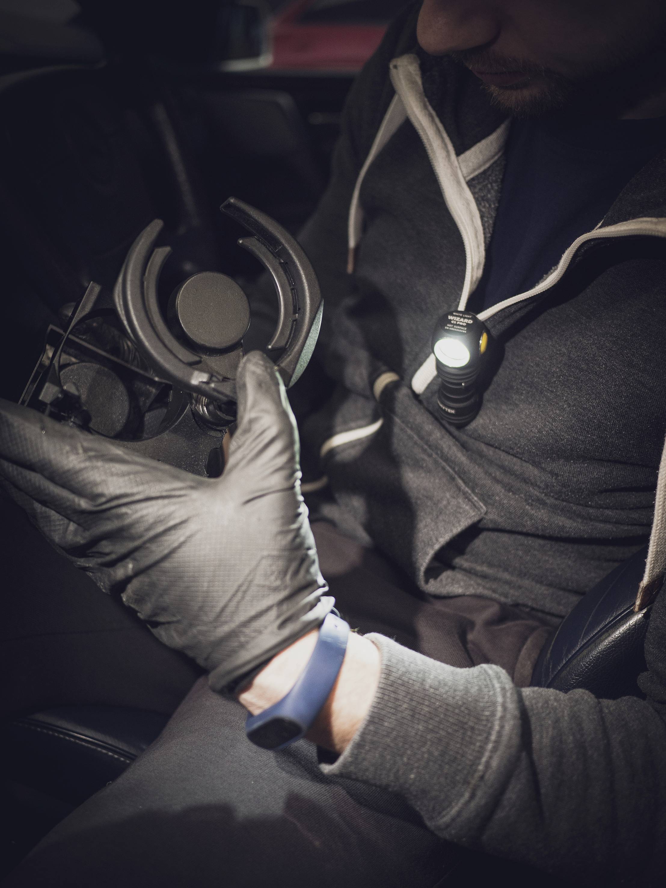 Eine Person in dunkler Kleidung prüft mit einer Stirnlampe und schwarzen Handschuhen ein rundes mechanisches Teil.