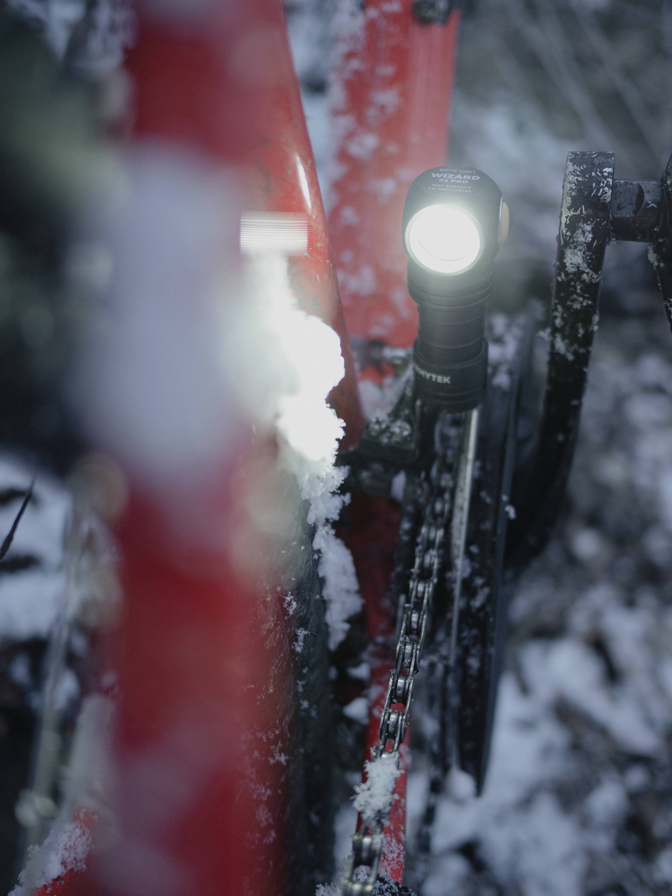 Nahaufnahme eines roten Fahrrads im Schnee, mit eingeschaltetem, hell leuchtendem Fahrradlicht.