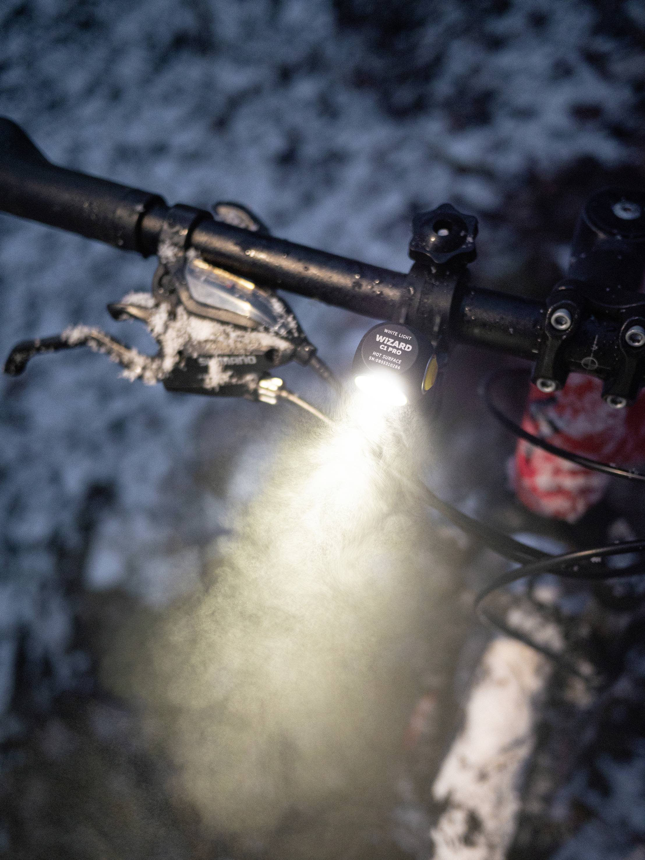 Fahrradlenker mit eingeschaltetem Licht in schneebedeckter Umgebung. Das Licht beleuchtet den Schnee deutlich.