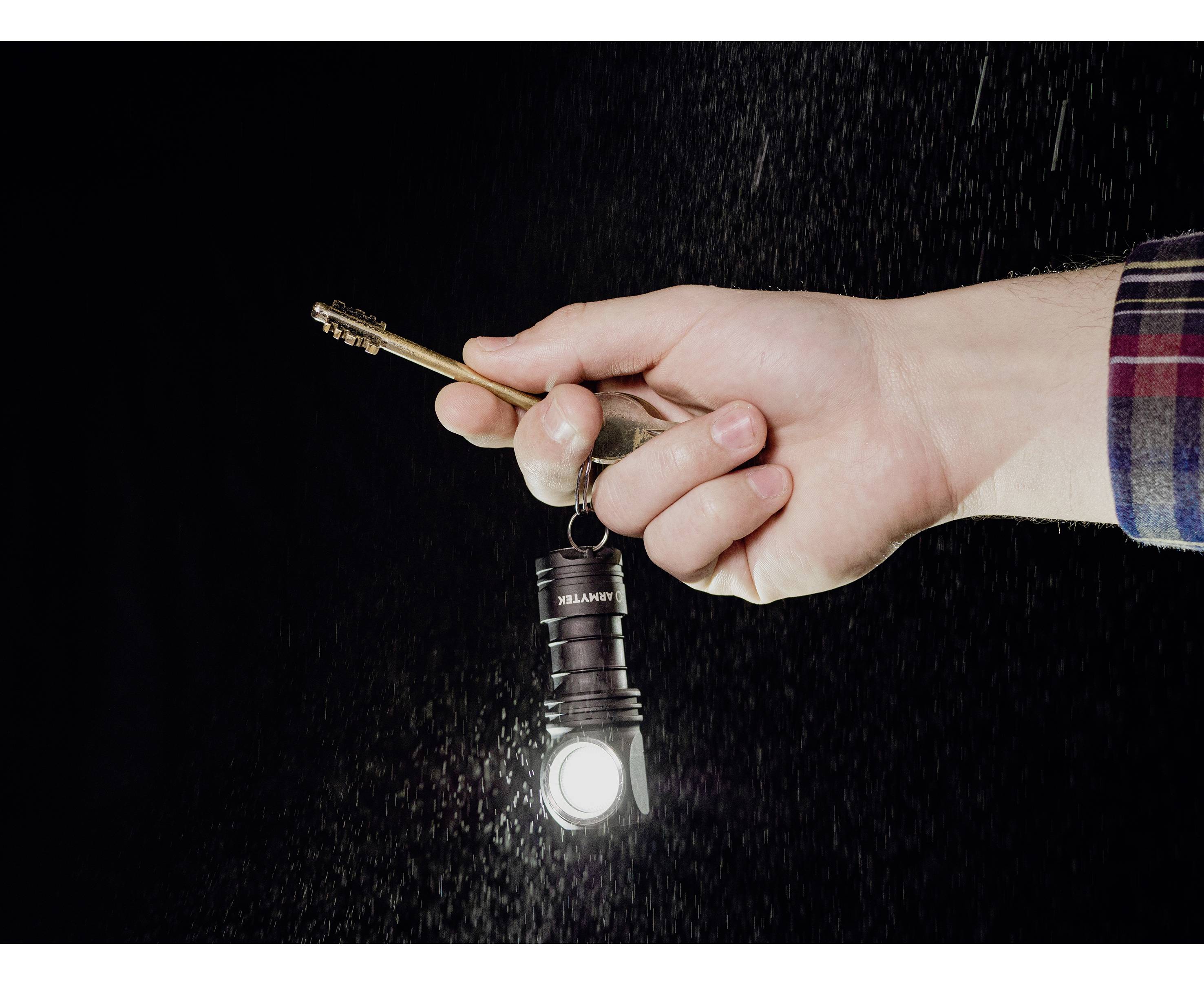 Eine Hand hält eine Taschenlampe und einen Schlüssel vor einem dunklen Hintergrund. Die Taschenlampe leuchtet stark.