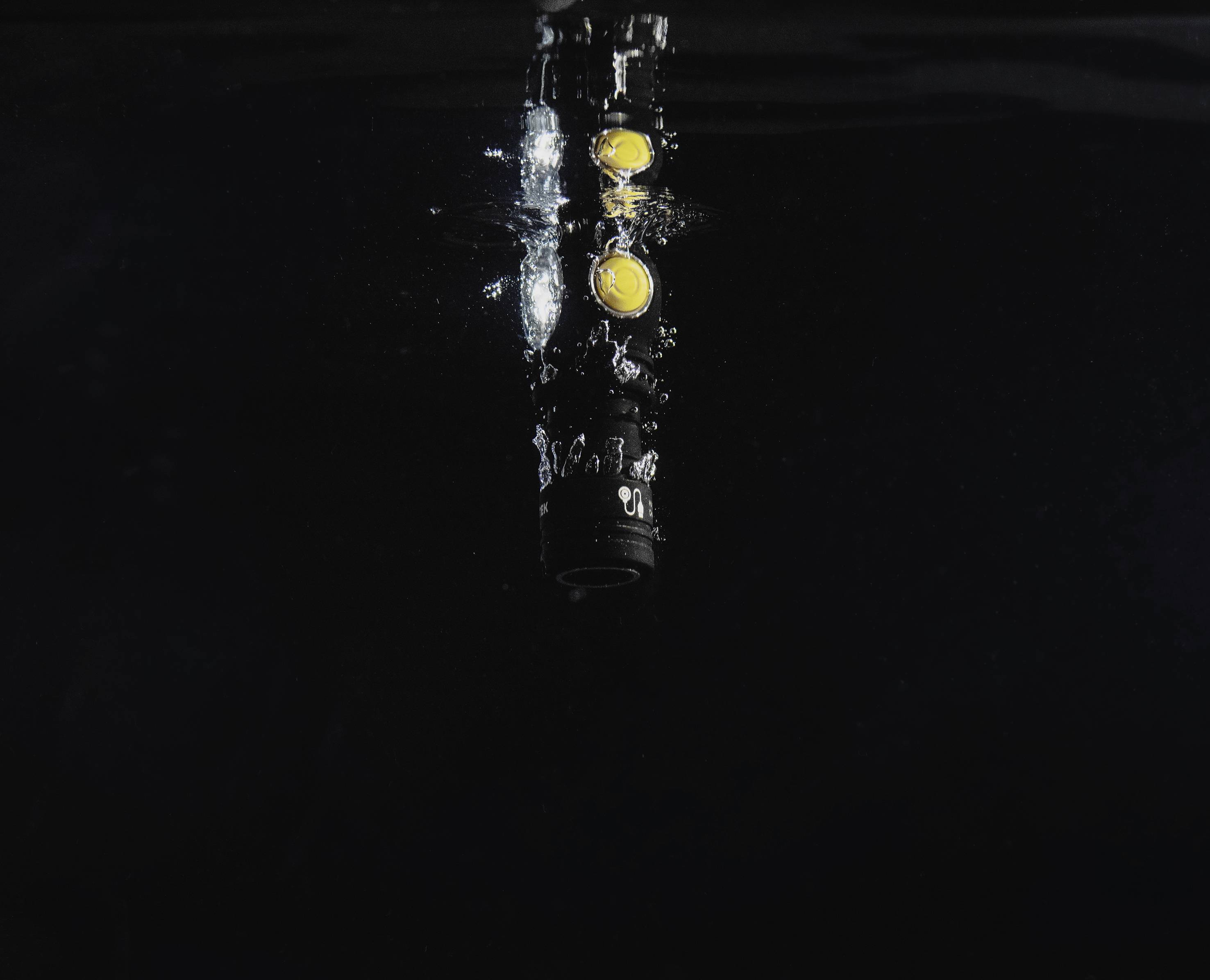 Taschenlampe leuchtet unter Wasser, Luftblasen steigen auf. Dunkler Hintergrund. Technologieszene, die Wasserdichtigkeit darstellt.