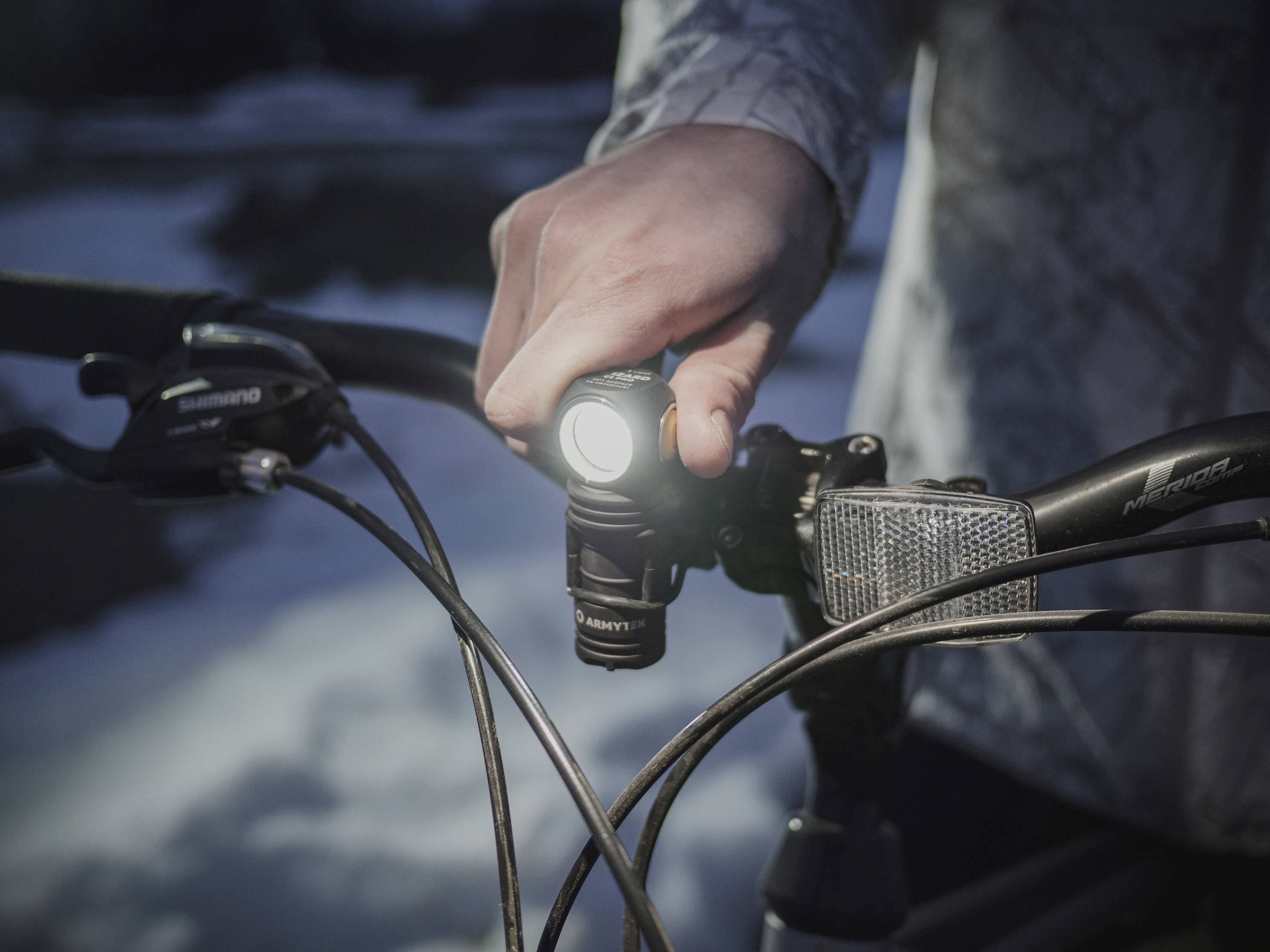 Eine Person schaltet eine Fahrradlampe ein. Das Fahrrad ist im Freien bei Nacht, was auf einen möglichen nächtlichen Fahrantritt hindeutet.