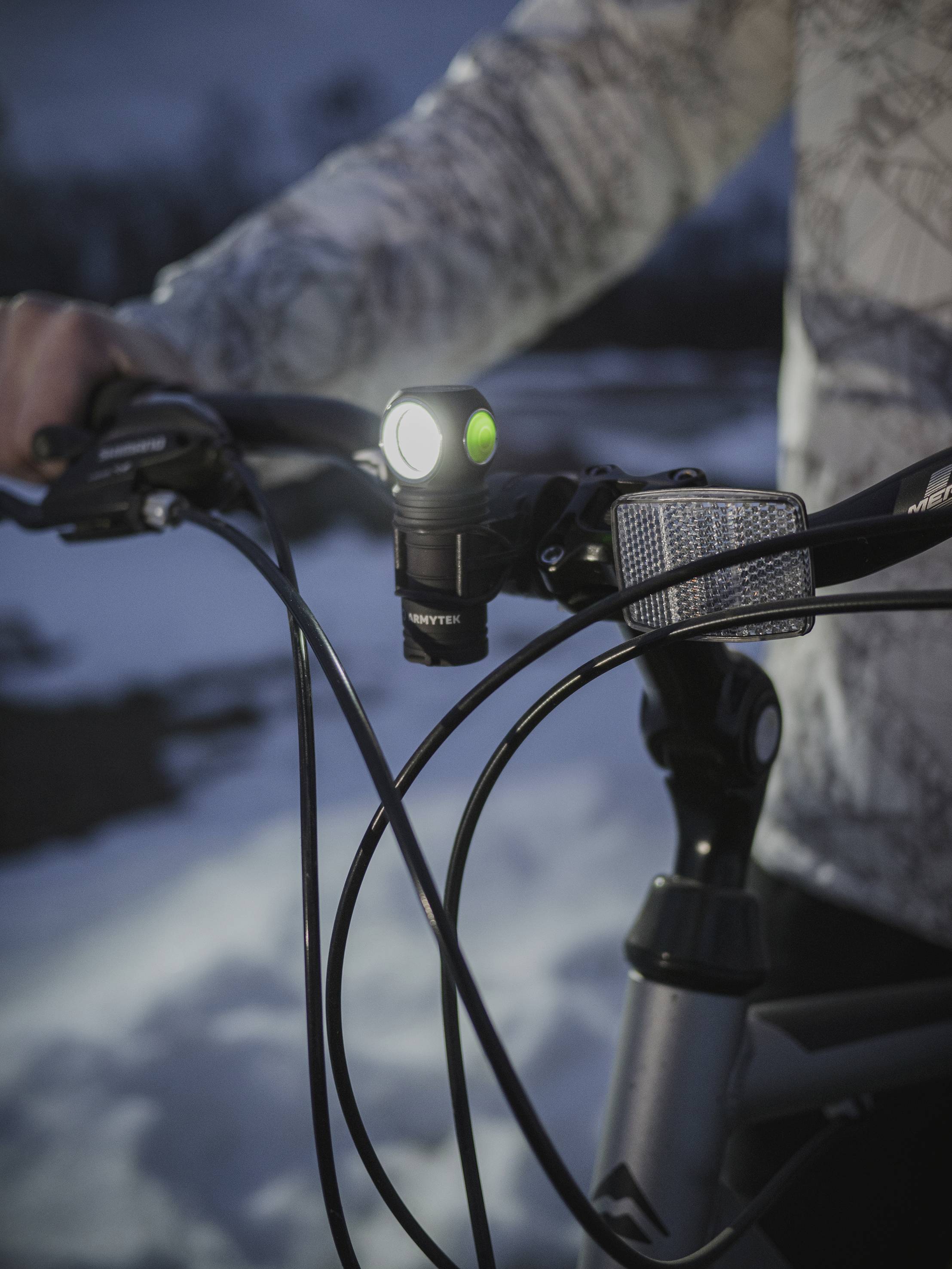 Ein Fahrradlenker im Schnee wird von einer Person gehalten. Ein helles Frontlicht ist eingeschaltet, beleuchtet den Weg.
