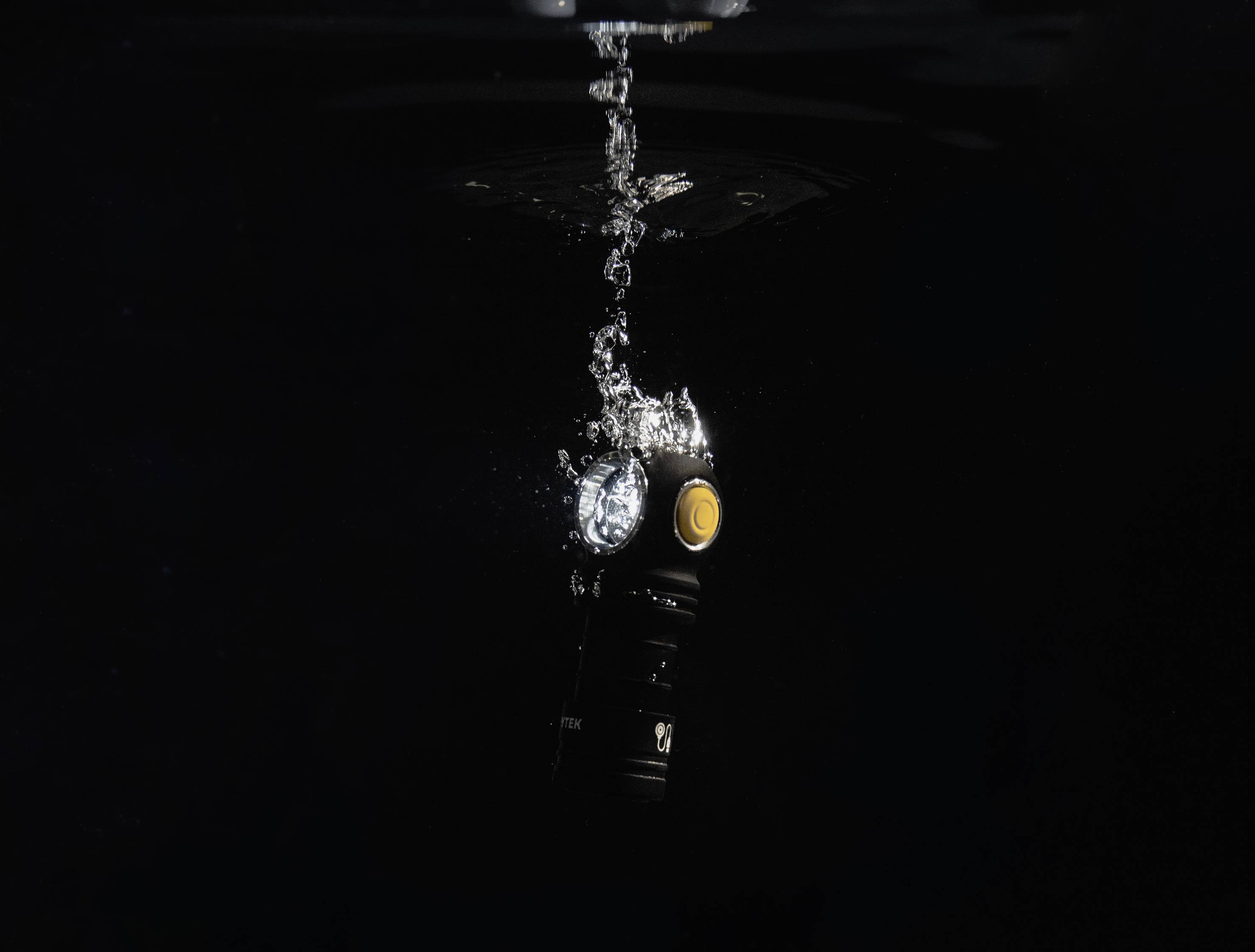 Taschenlampe unter Wasser mit Blasen, die aufsteigen; schwaches Licht in dunkler Umgebung.