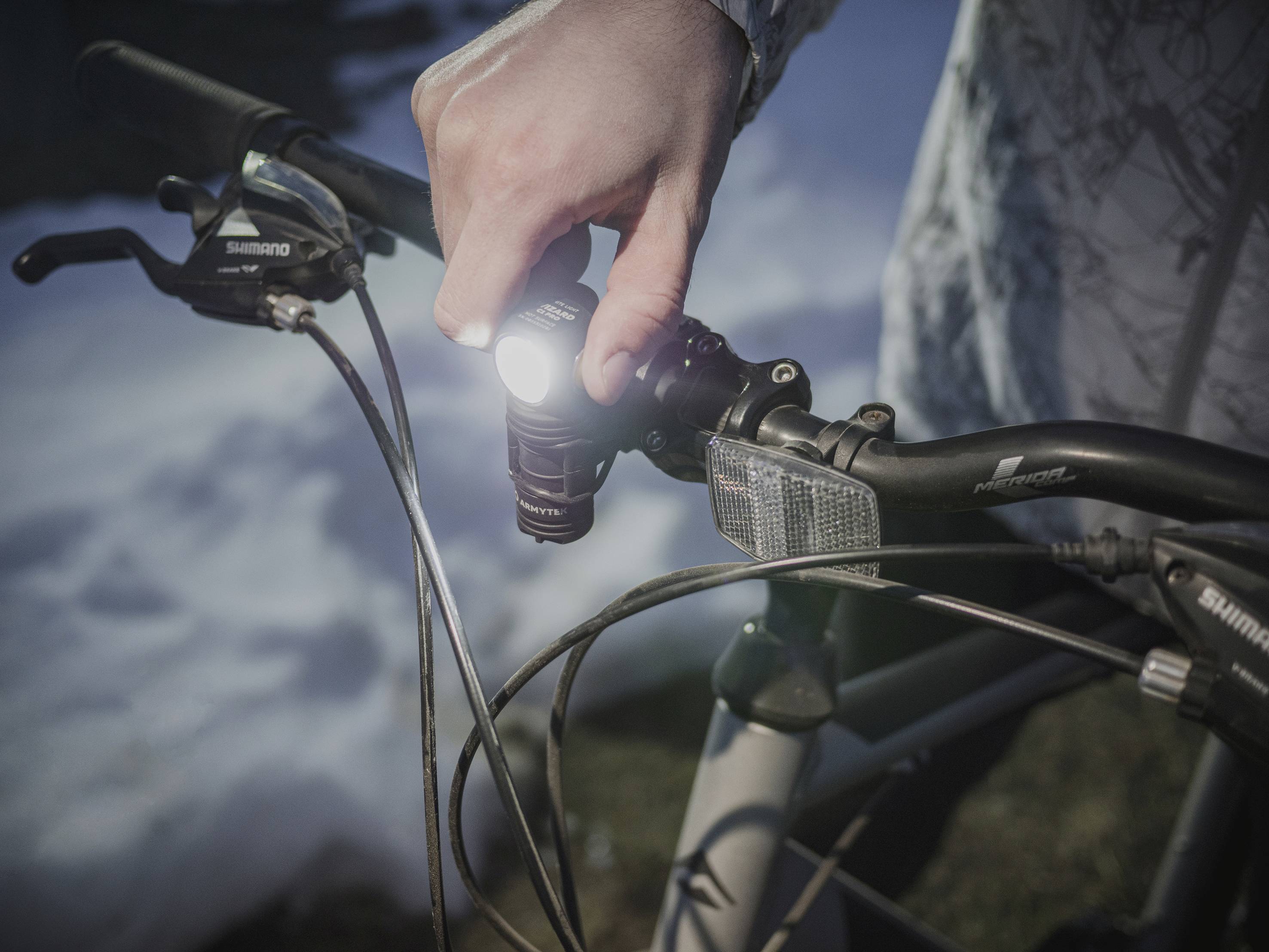 Person hält Fahrradlenker mit eingeschaltetem Licht in dunkler Umgebung. Schneebedeckter Boden im Hintergrund.
