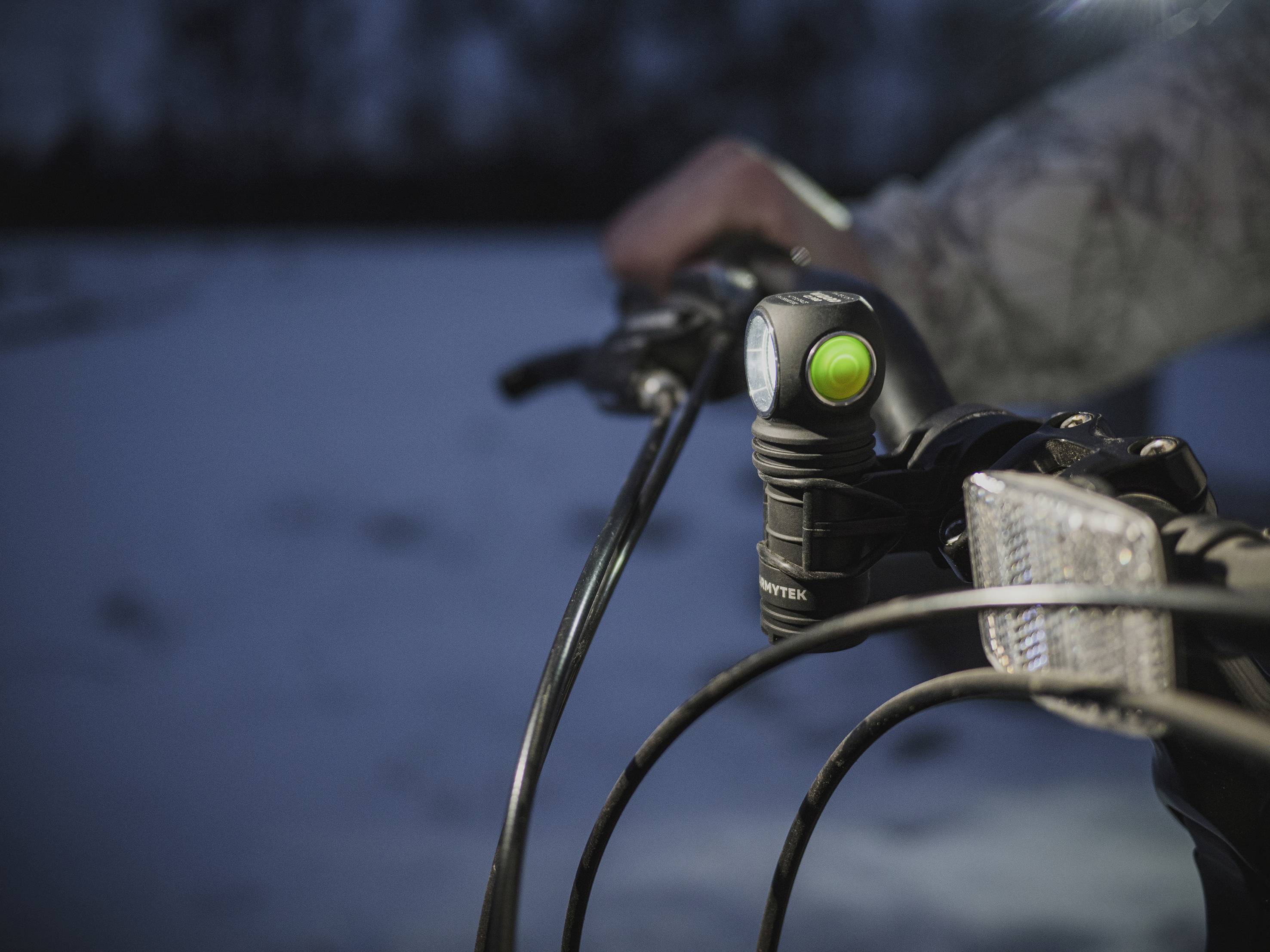 Nahaufnahme eines Fahrrads im Dunkeln mit eingeschaltetem Vorderlicht. Eine Hand hält den Lenker. Im Hintergrund ist Schnee sichtbar.