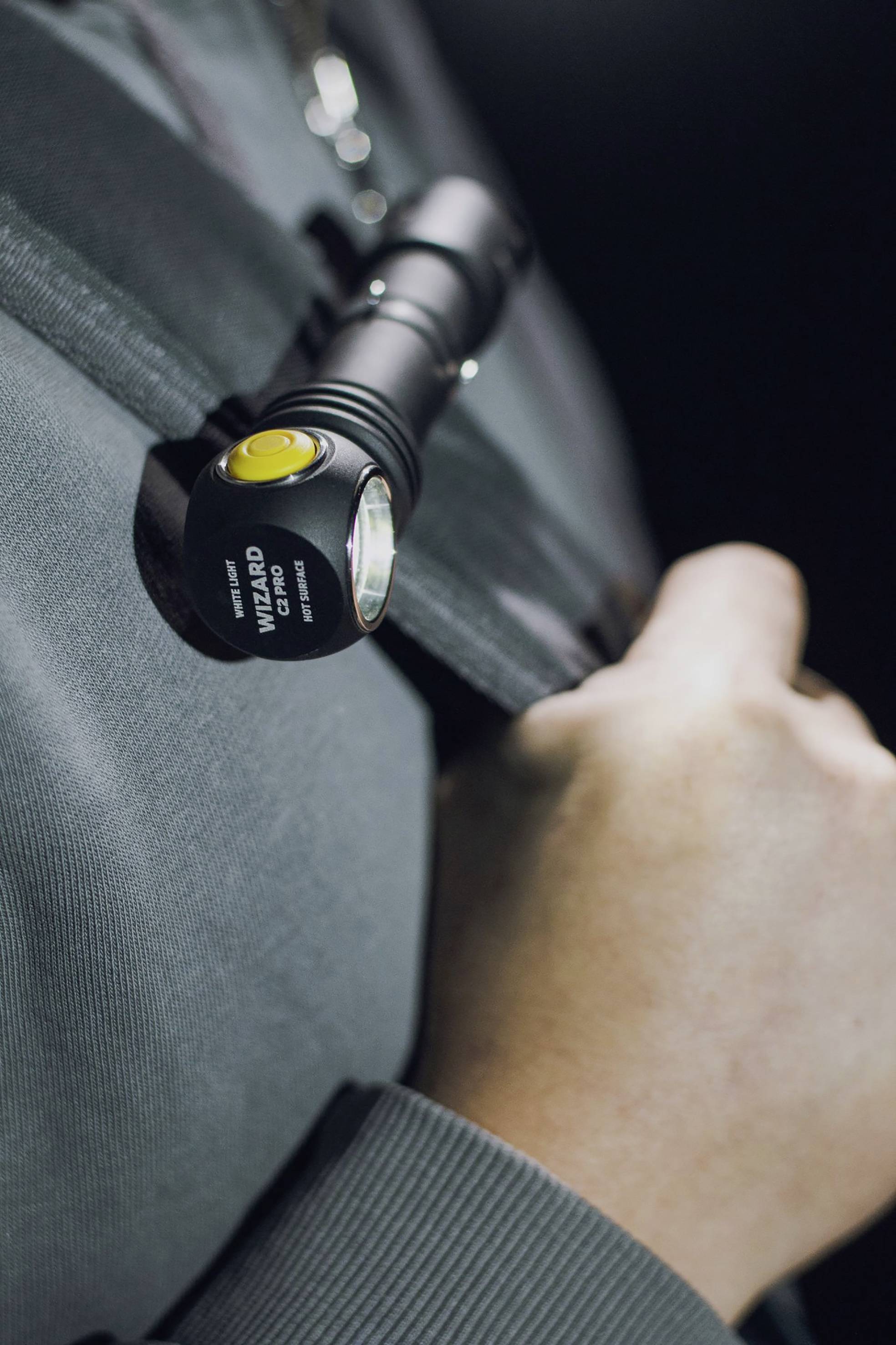 Eine Person hält eine Taschenlampe, die an einem Gürtel befestigt ist. Die Hand zeigt auf die rechte Seite der Lampe.