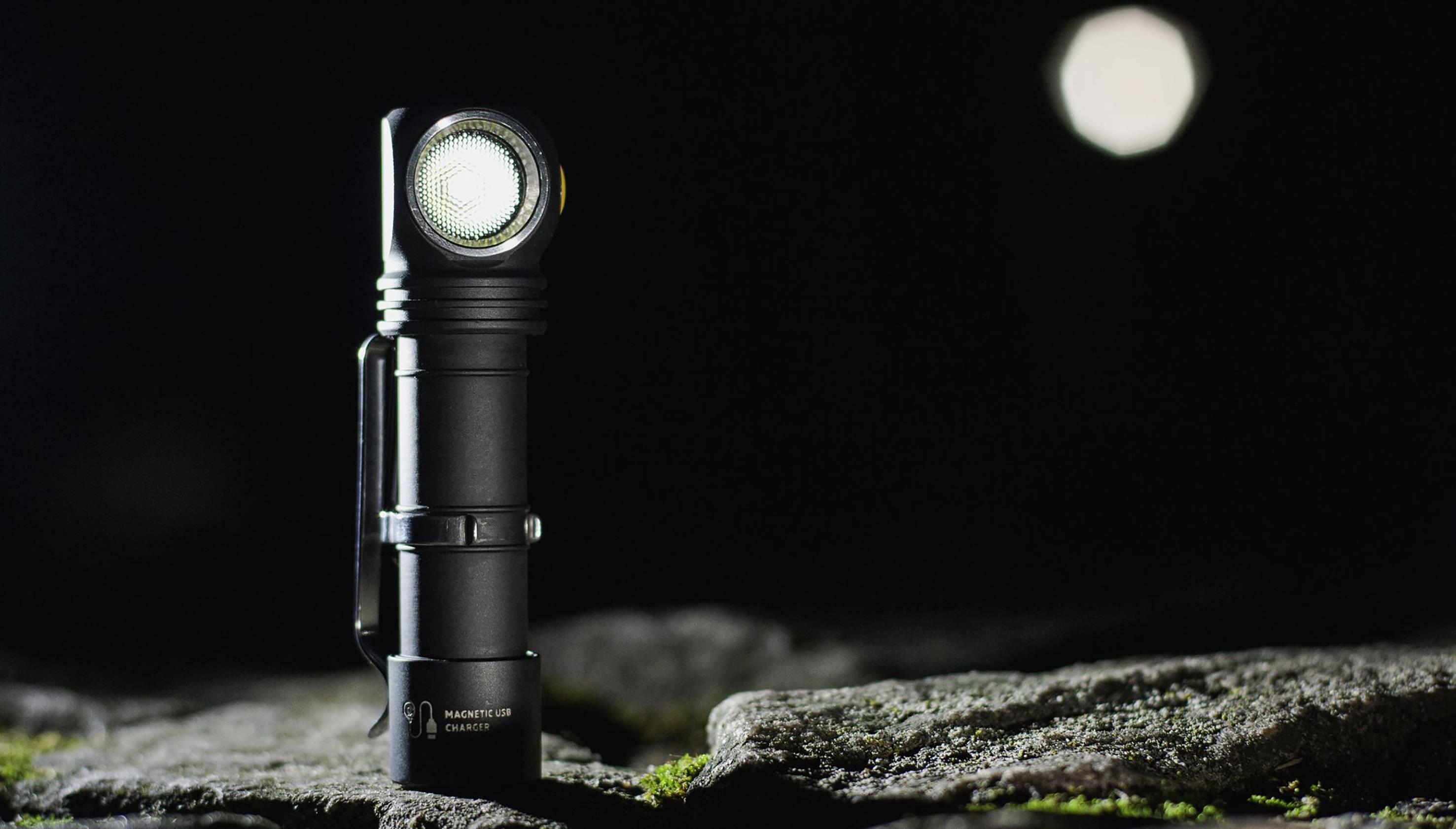 Eine schwarze Taschenlampe mit hellem Licht steht auf einem felsigen Untergrund im Dunkeln, beleuchtet von oben.