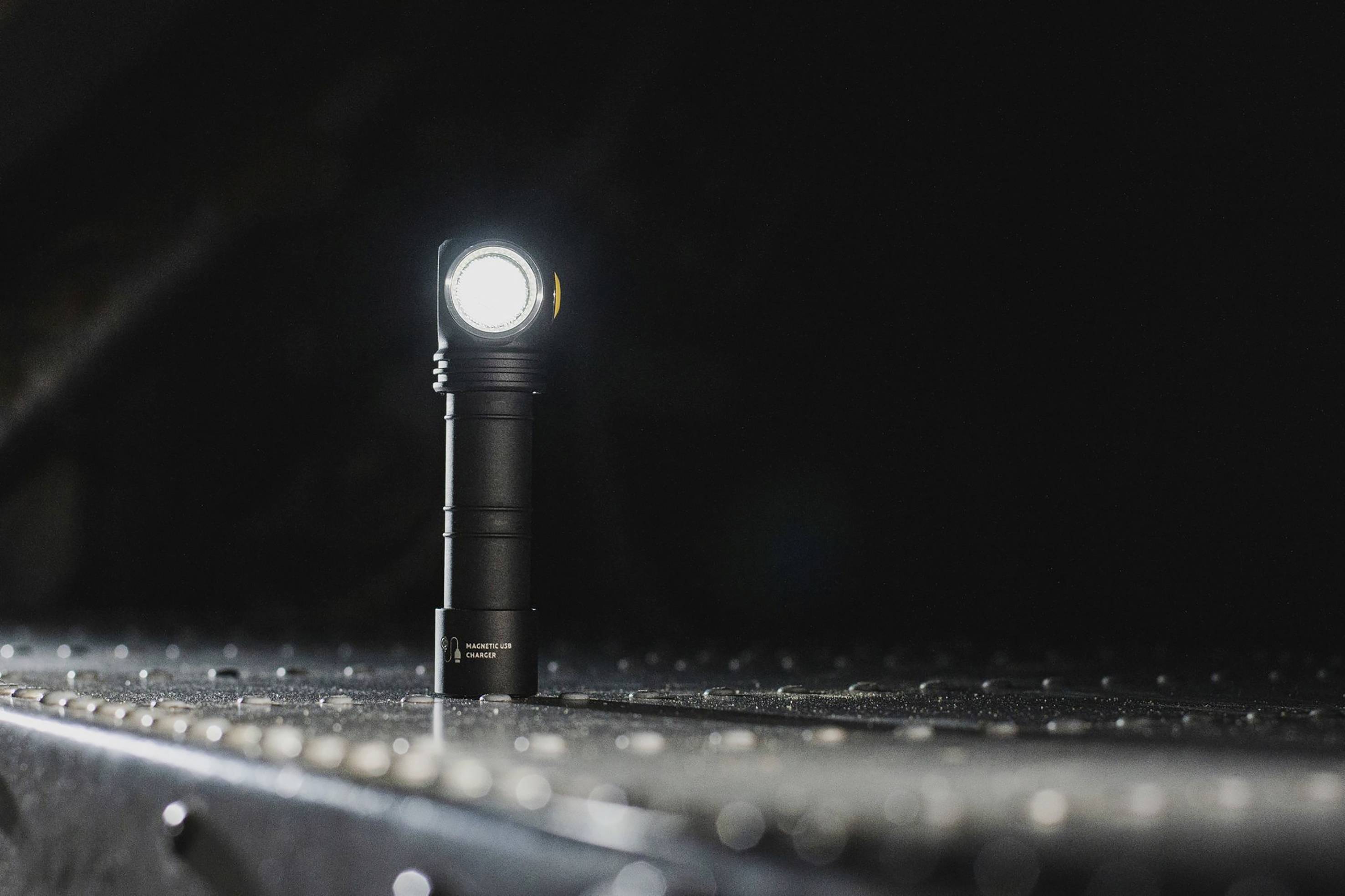 Taschenlampe leuchtet in dunklem Raum, stehend auf metallischer Oberfläche. Sie strahlt helles Licht aus, hebt sich von der Dunkelheit ab.