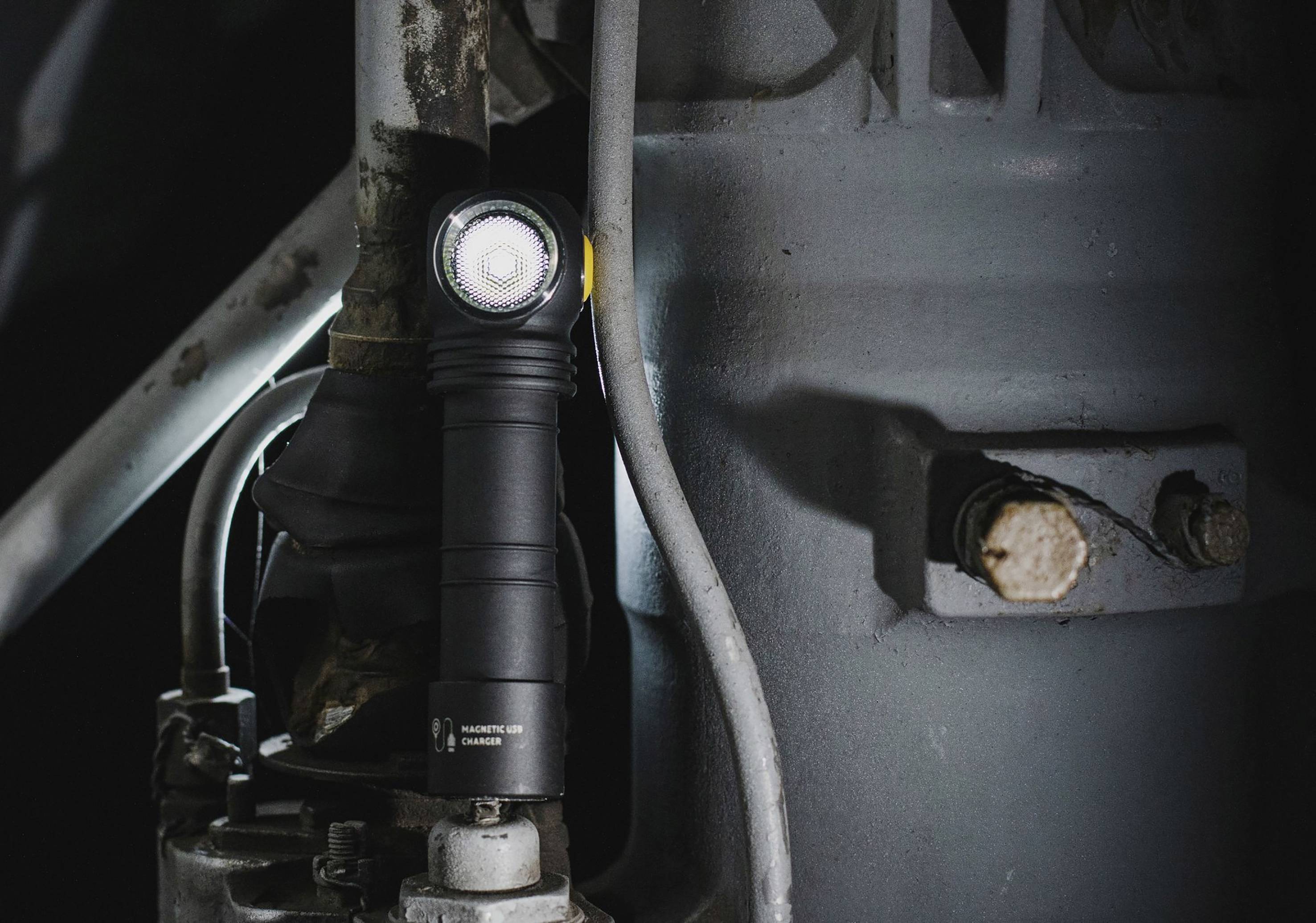 Taschenlampe leuchtet in einem dunklen, industriellen Raum, fixiert an einem Metallrohr. Sie bietet fokussiertes Licht auf die Umgebung.