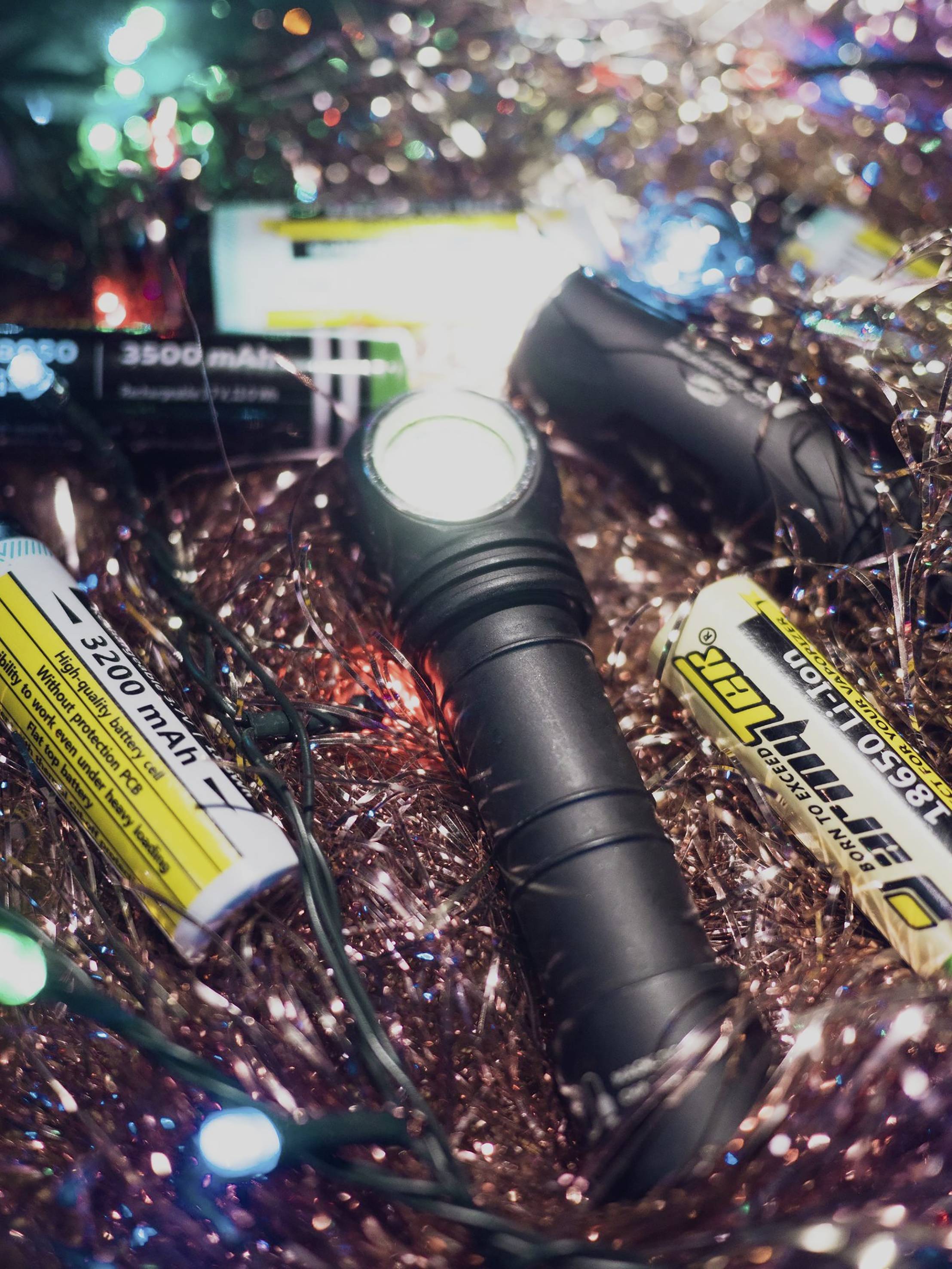 Eine Taschenlampe liegt inmitten von glänzendem, buntem Lametta und Lichterketten, umgeben von Batterien.