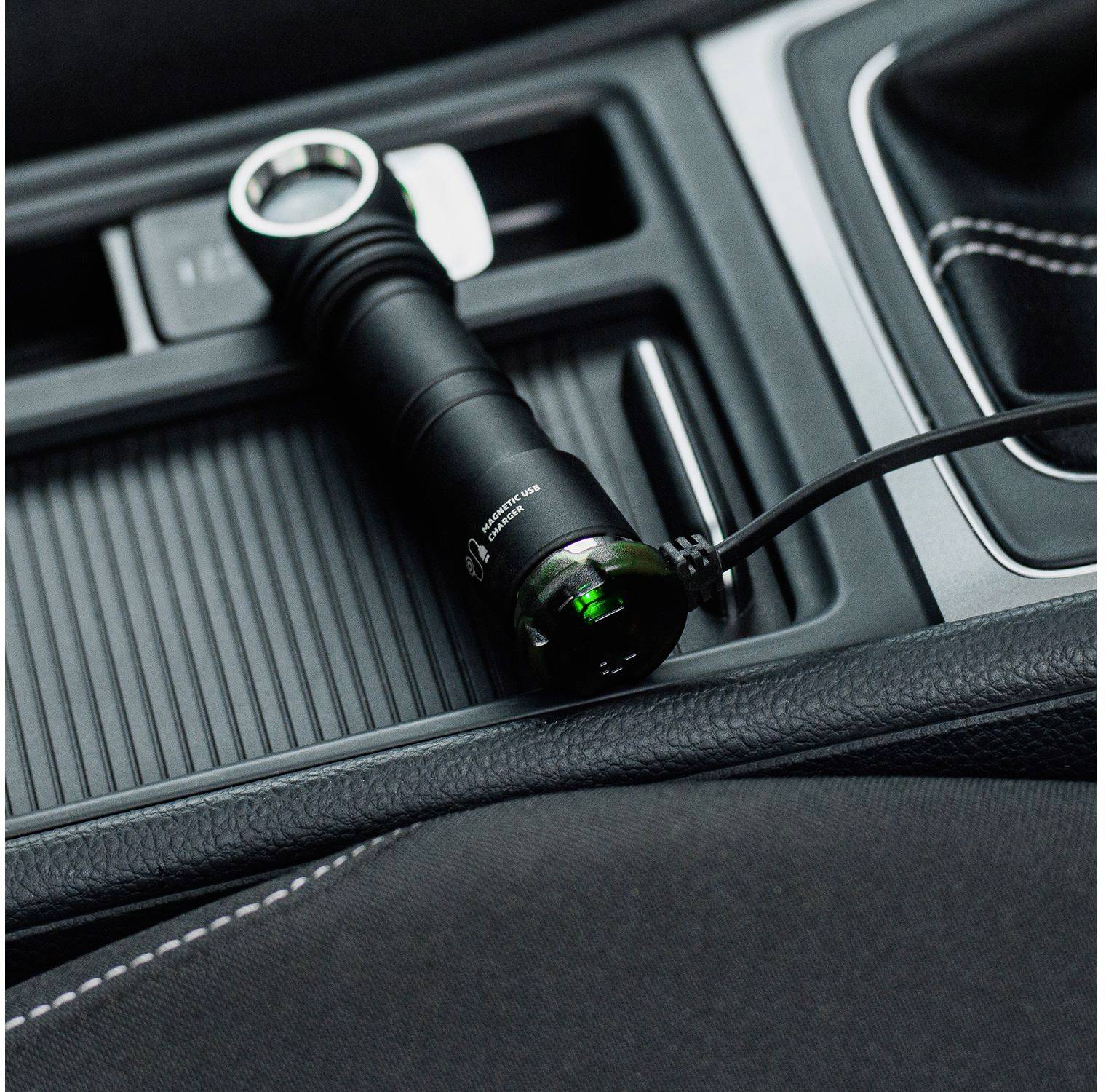 Taschenlampe wird im Auto-Getränkehalter aufgeladen, verbunden mit einem USB-Kabel. Innenraum eines Fahrzeugs mit schwarzen Sitzen.