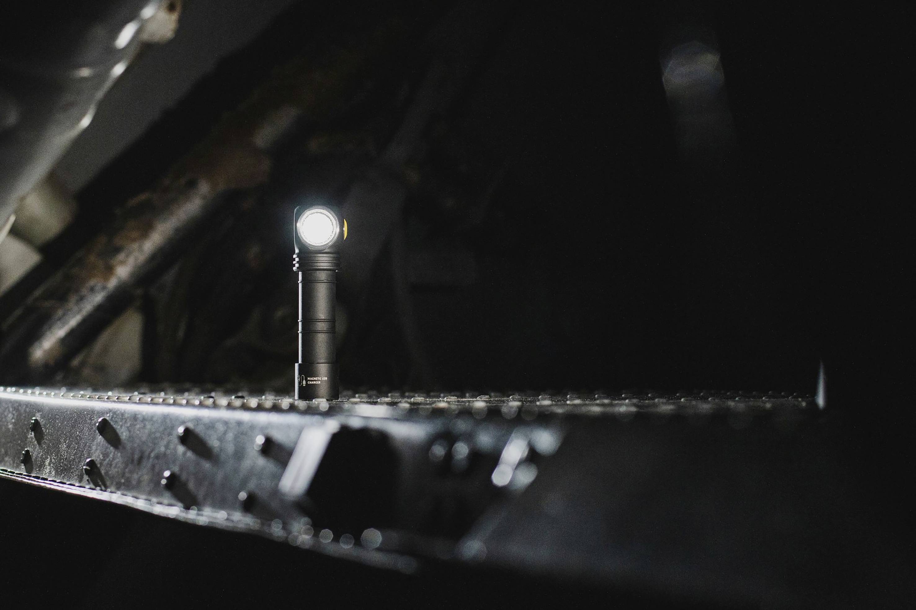 Eine leuchtende Taschenlampe steht auf einer metallischen, geriffelten Oberfläche in einer dunklen Umgebung.