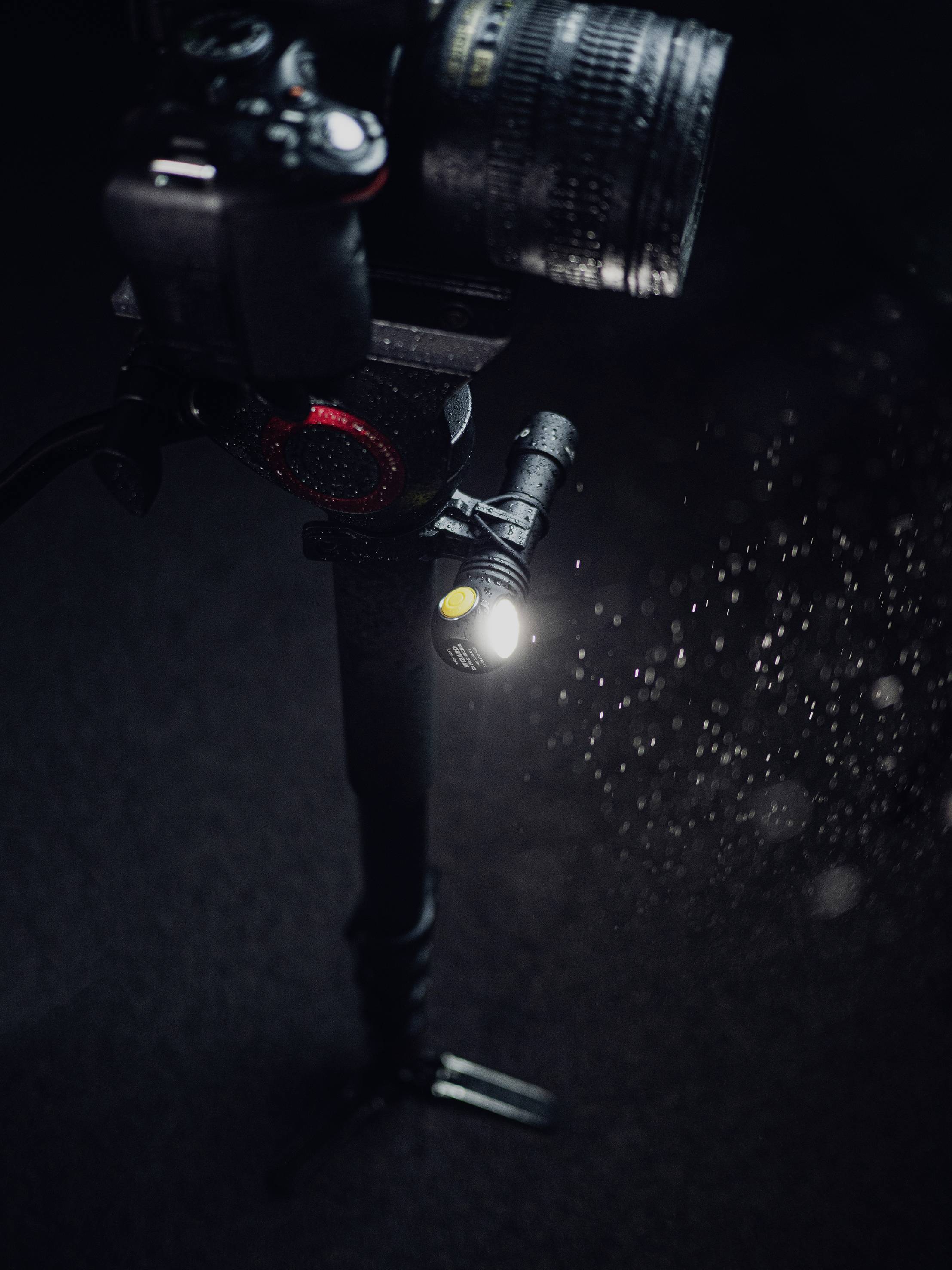 Kamera auf einem Stativ mit einem montierten Objektiv, umgeben von sprühenden Wassertropfen, die im Licht glitzern.