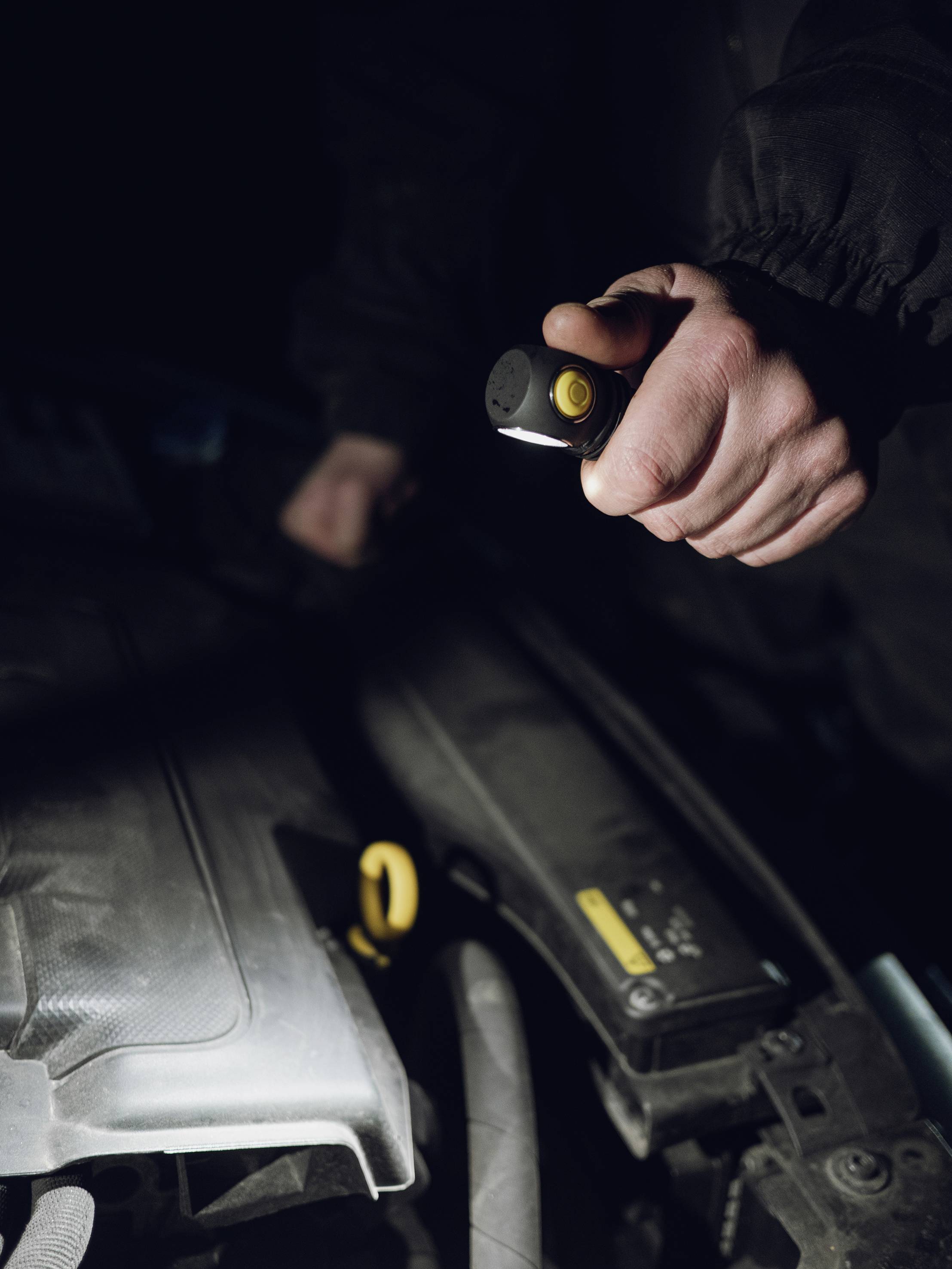 Ein Mechaniker untersucht mit einer Taschenlampe den Motorraum eines Autos bei wenig Licht.