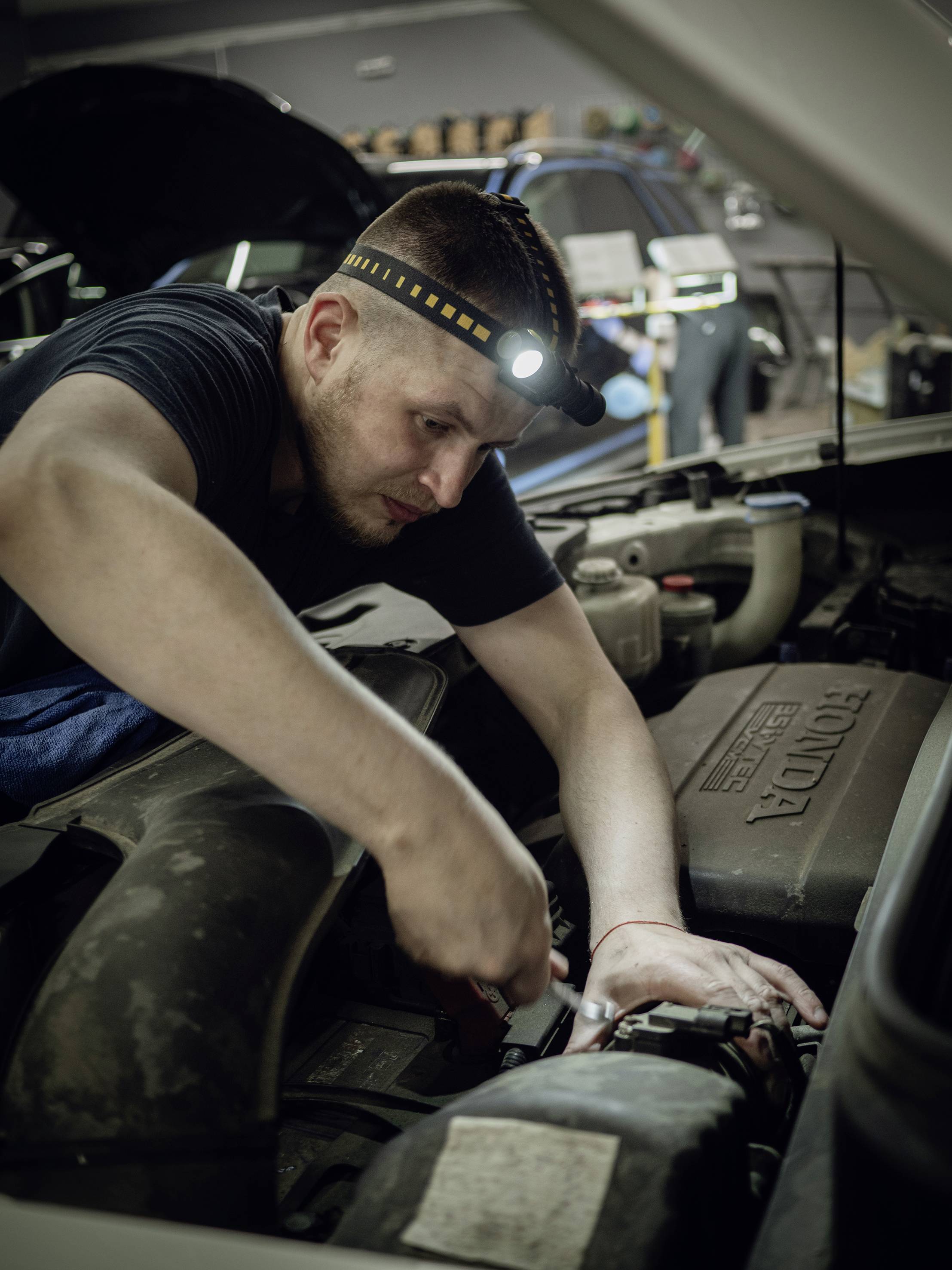 Ein Mechaniker repariert einen Motor in einer Autowerkstatt. Er trägt ein Stirnlicht, um den Motorraum zu beleuchten.
