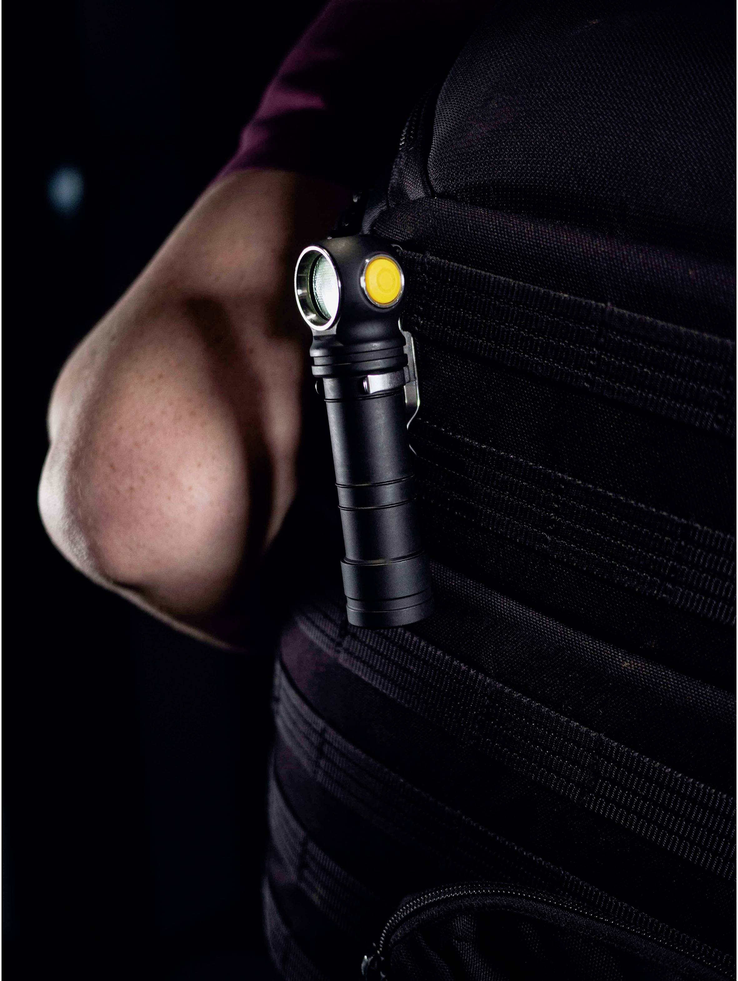 Eine kleine, schwarze LED-Taschenlampe mit gelbem Knopf ist seitlich an einem schwarzen Rucksack befestigt.