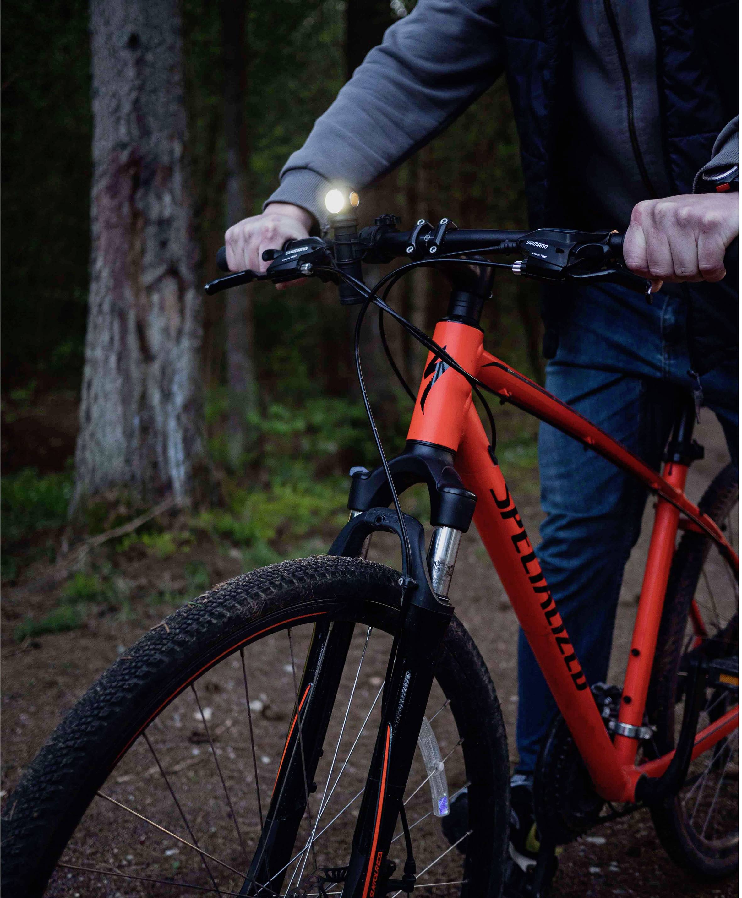 Eine Person fährt ein rotes Fahrrad auf einem Waldweg. Der Scheinwerfer des Fahrrads ist eingeschaltet.