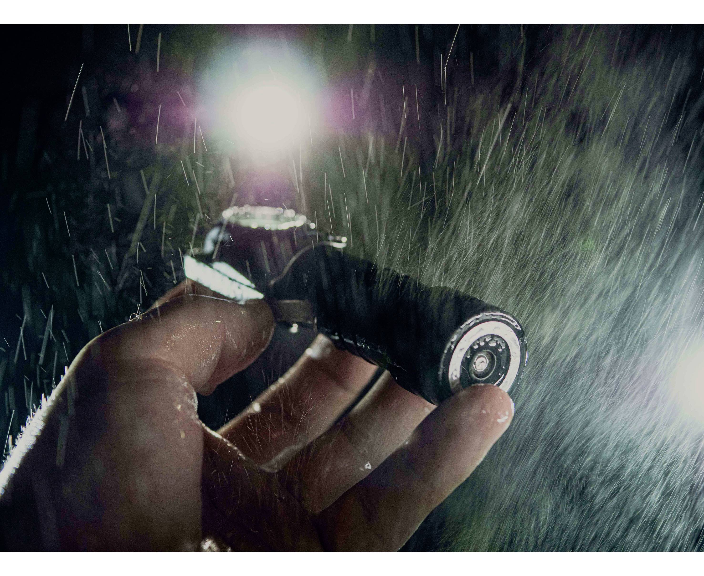 Hand hält Kamera im Regen, beleuchtet von zwei Lichtquellen, betont die Robustheit der Kamera.