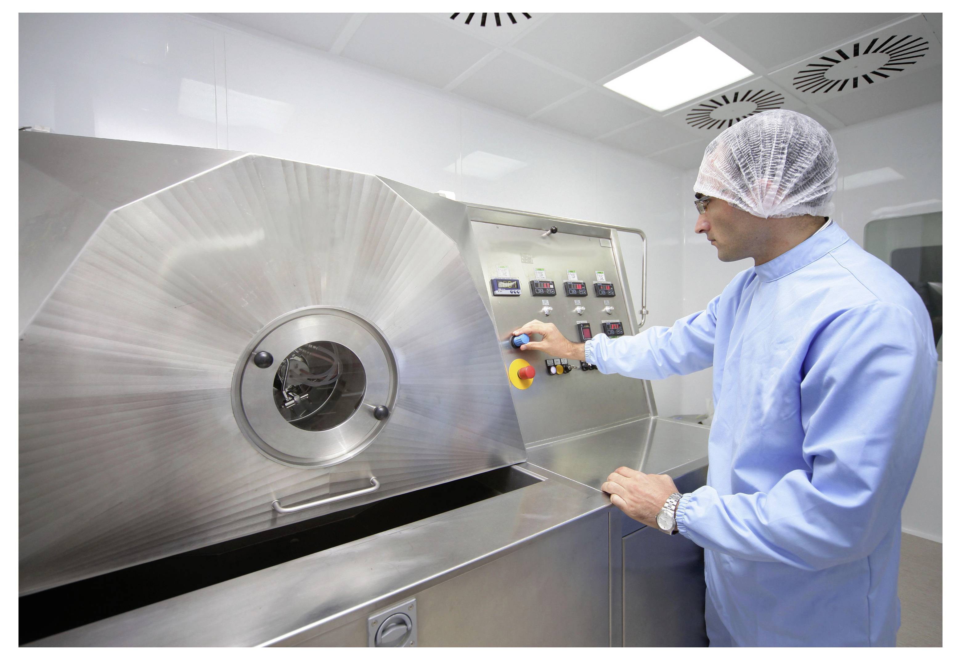 Techniker in Schutzkleidung bedient eine große Edelstahl-Industriemaschine in einem Reinraum oder pharmazeutischen Verarbeitungsbereich.