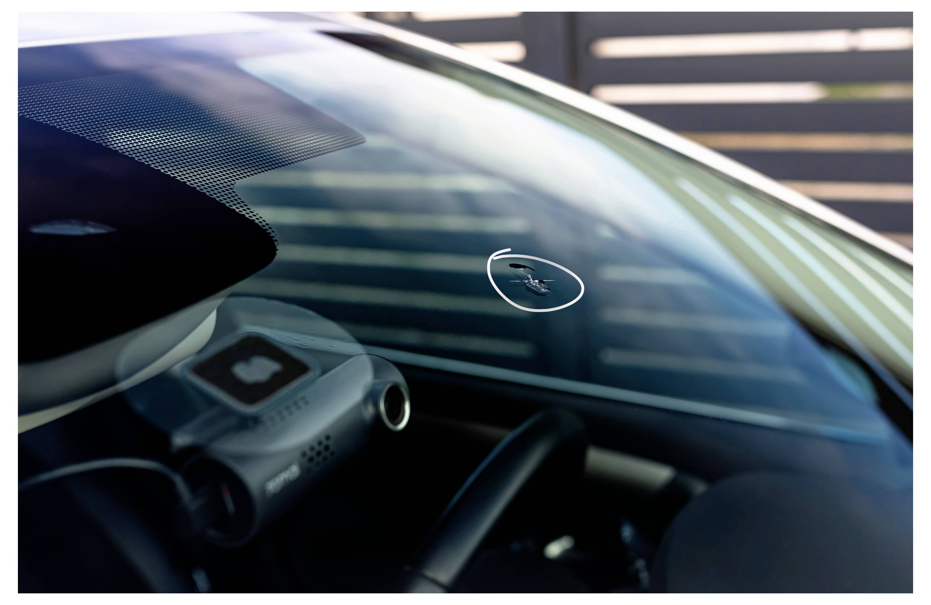 Nahaufnahme durch eine Autowindschutzscheibe, die einen kleinen kreisförmigen Aufkleber oder Sensor in der Nähe der Mitte zeigt, mit dem Armaturenbrett im Inneren sichtbar.