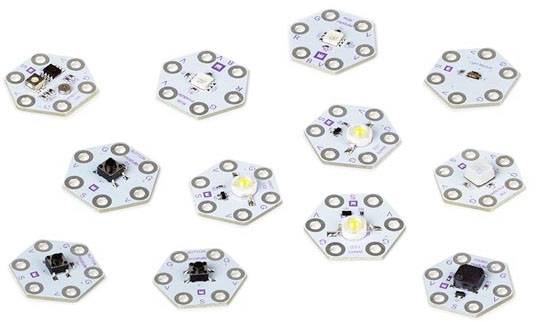 Elf sechseckige Platinen mit unterschiedlichen elektronischen Komponenten und LEDs, auf weißem Hintergrund verstreut.