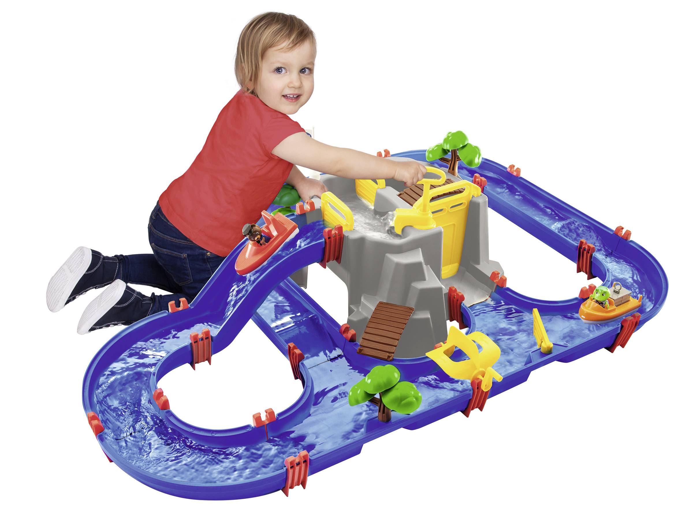 Ein Kind spielt lächelnd mit einer blauen Wasserbahn, die Boote und Schleusen umfasst. Es trägt ein rotes Shirt und sitzt auf dem Boden.