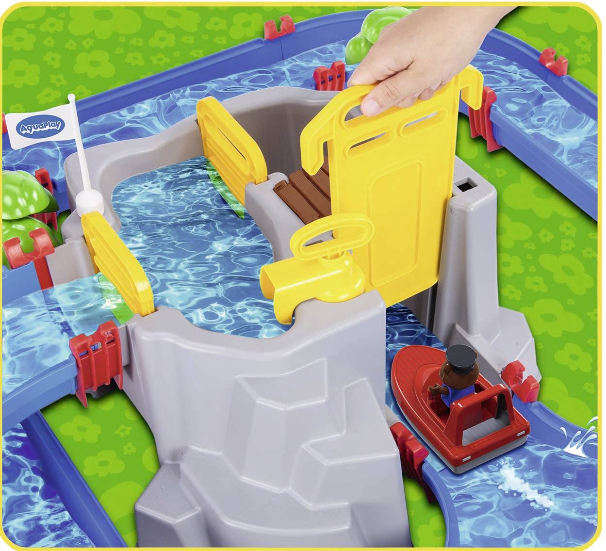 Spielzeugkanal mit Wasser, Schleusentoren und rotem Boot. Eine Hand hält das gelbe Tor. Kinder entdecken Wasserbewegung spielerisch.