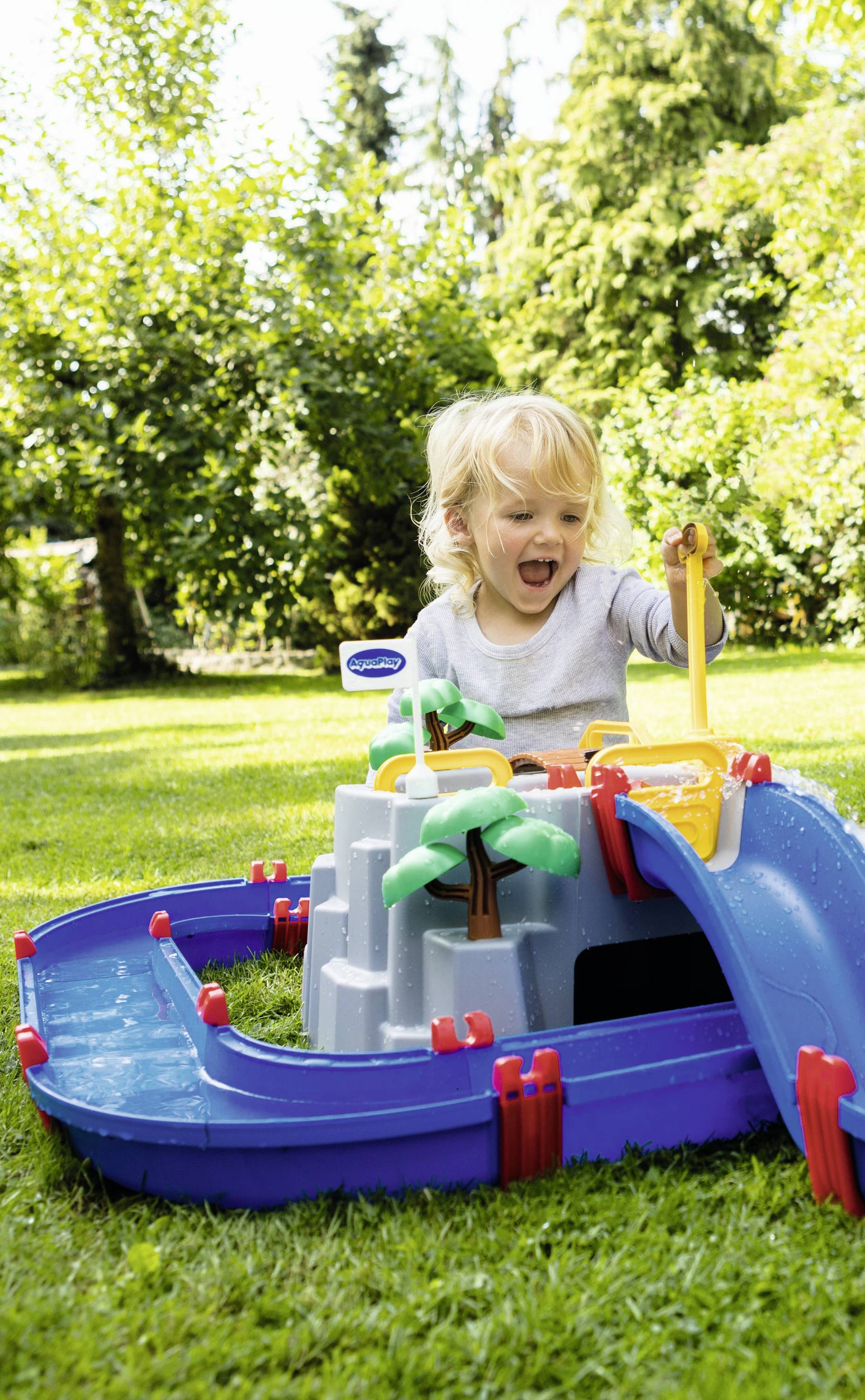 Ein Kind spielt freudig mit einem bunten Wasserspielzeug im Garten. Bäume und Gras im Hintergrund.