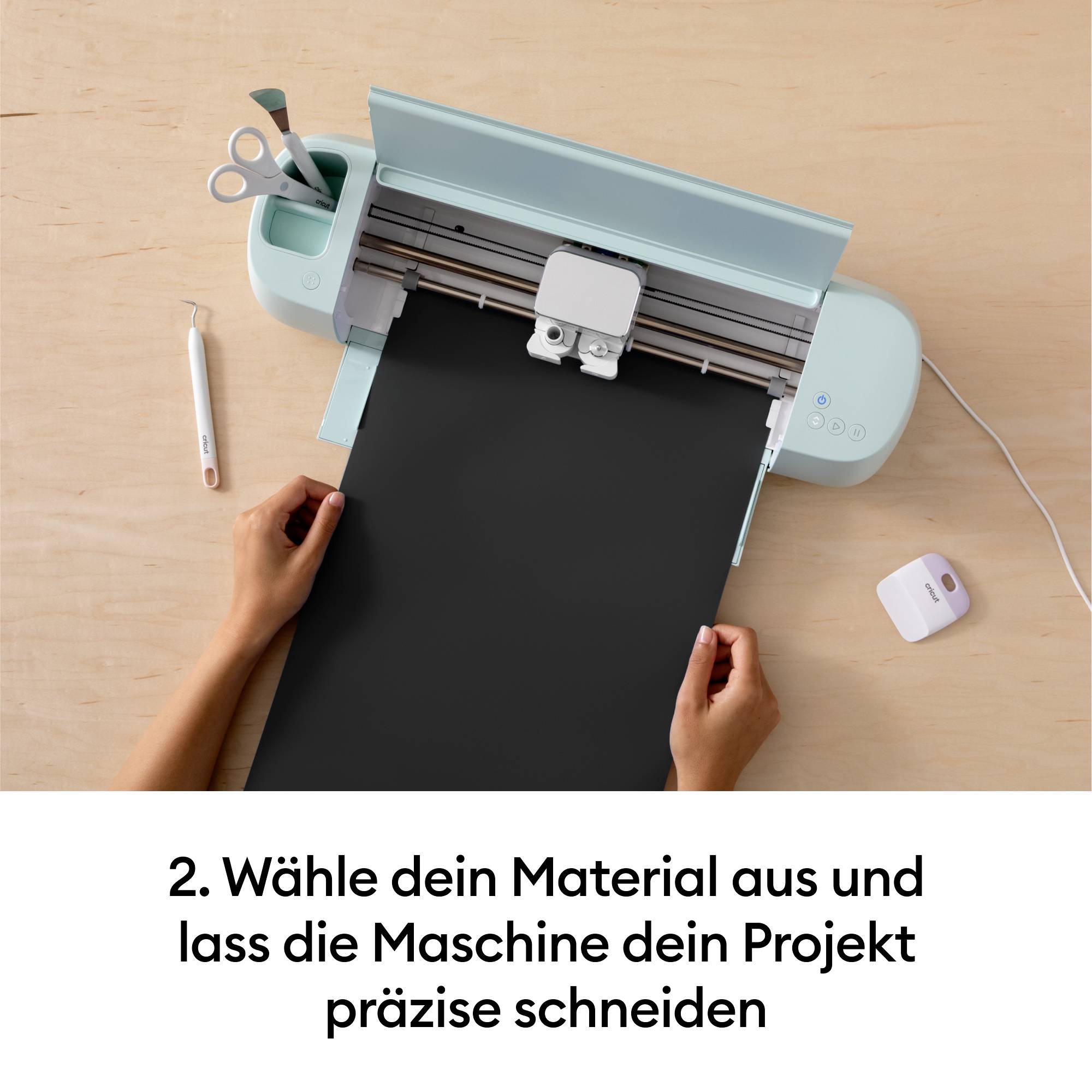 Eine Person benutzt eine Schneidemaschine, um ein schwarzes Material präzise zu schneiden. Text unten: 'Wähle dein Material aus und lass die Maschine dein Projekt präzise schneiden'.