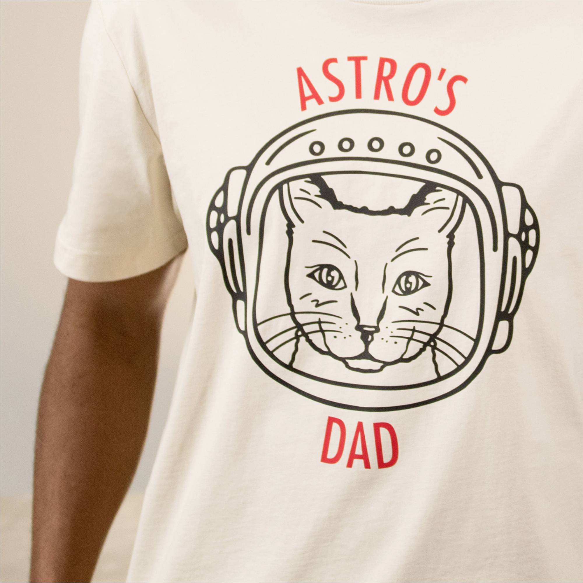 Ein T-Shirt mit einem Katzenkopf in einem Astronautenhelm und der Aufschrift 'ASTRO'S DAD'.
