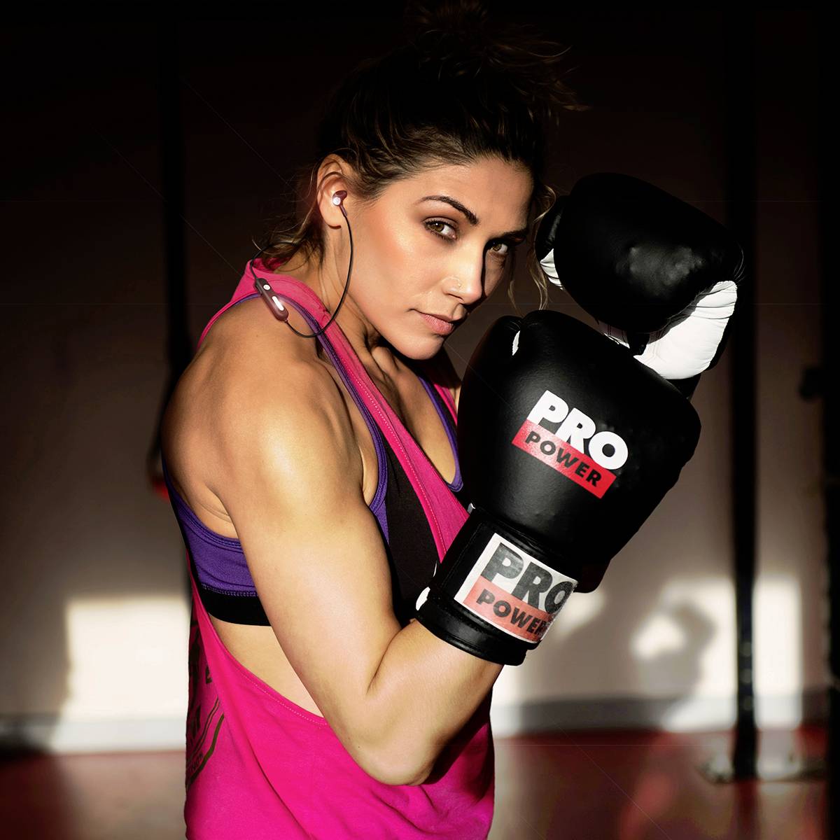 Eine Person in Sportkleidung hält Boxhandschuhe und posiert in einem Fitnessstudio, bereit zum Boxen. Sie wirkt fokussiert und stark.