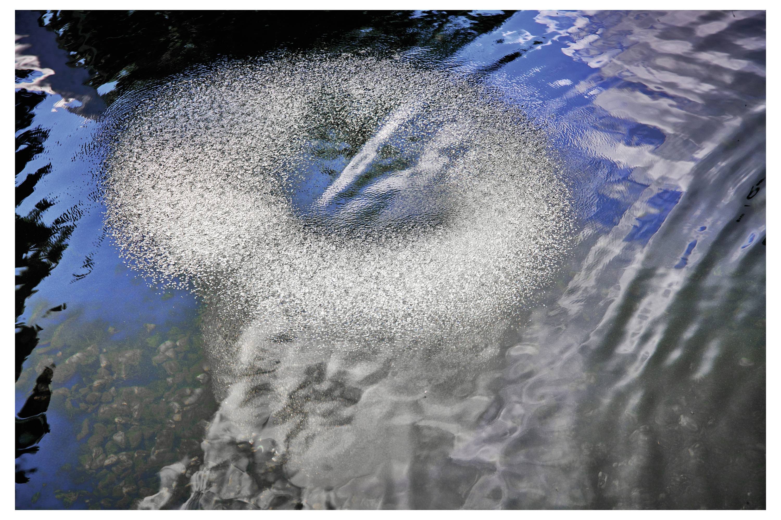 Ein kreisförmiges Muster von Blasen im Wasser, die das Licht reflektieren und einen wirbelnden Effekt erzeugen.