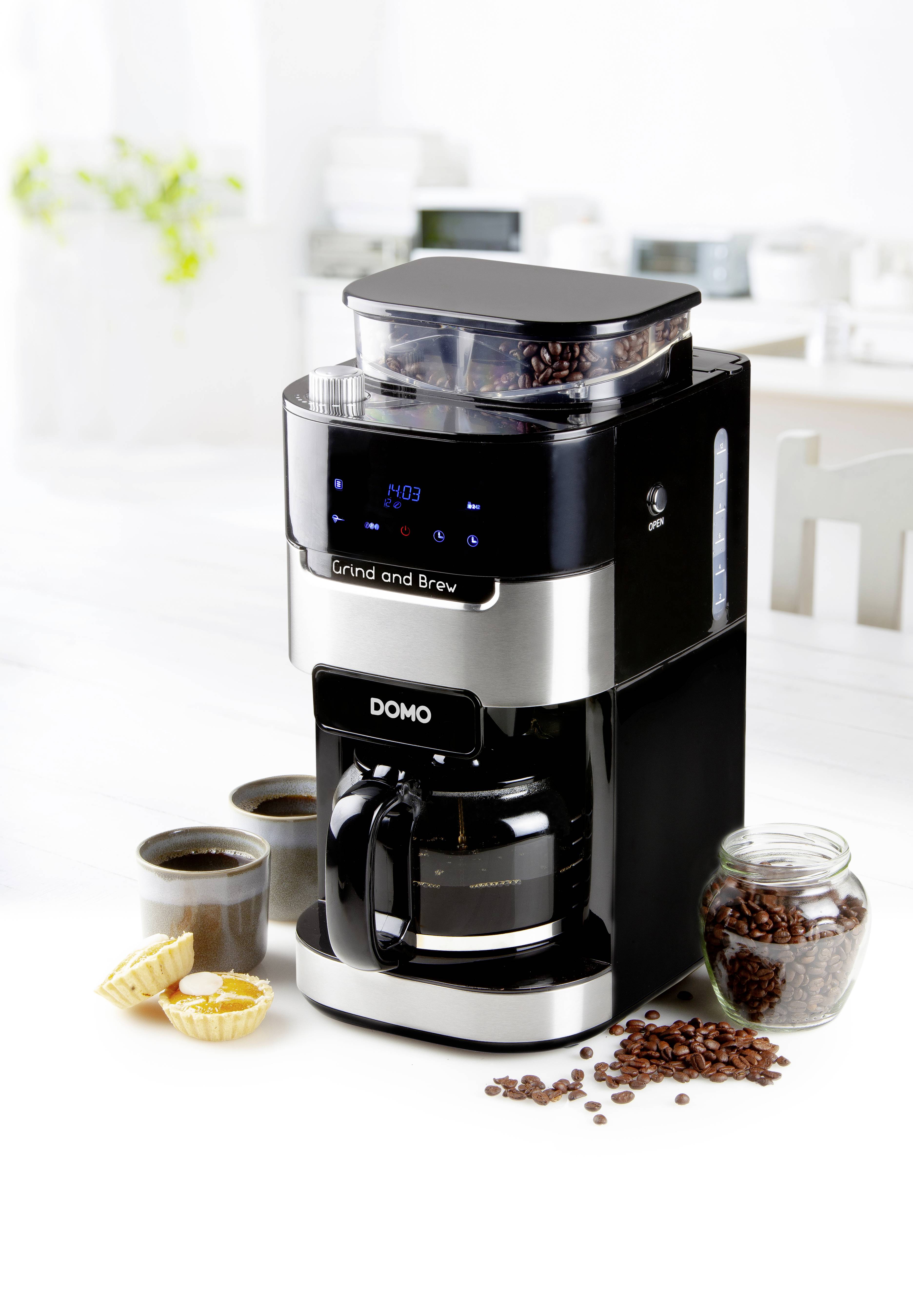 Eine schwarze Kaffeemaschine mit integriertem Mahlwerk, gefüllter Kaffeekanne und Kaffeebohnen daneben; moderne Küche im Hintergrund.