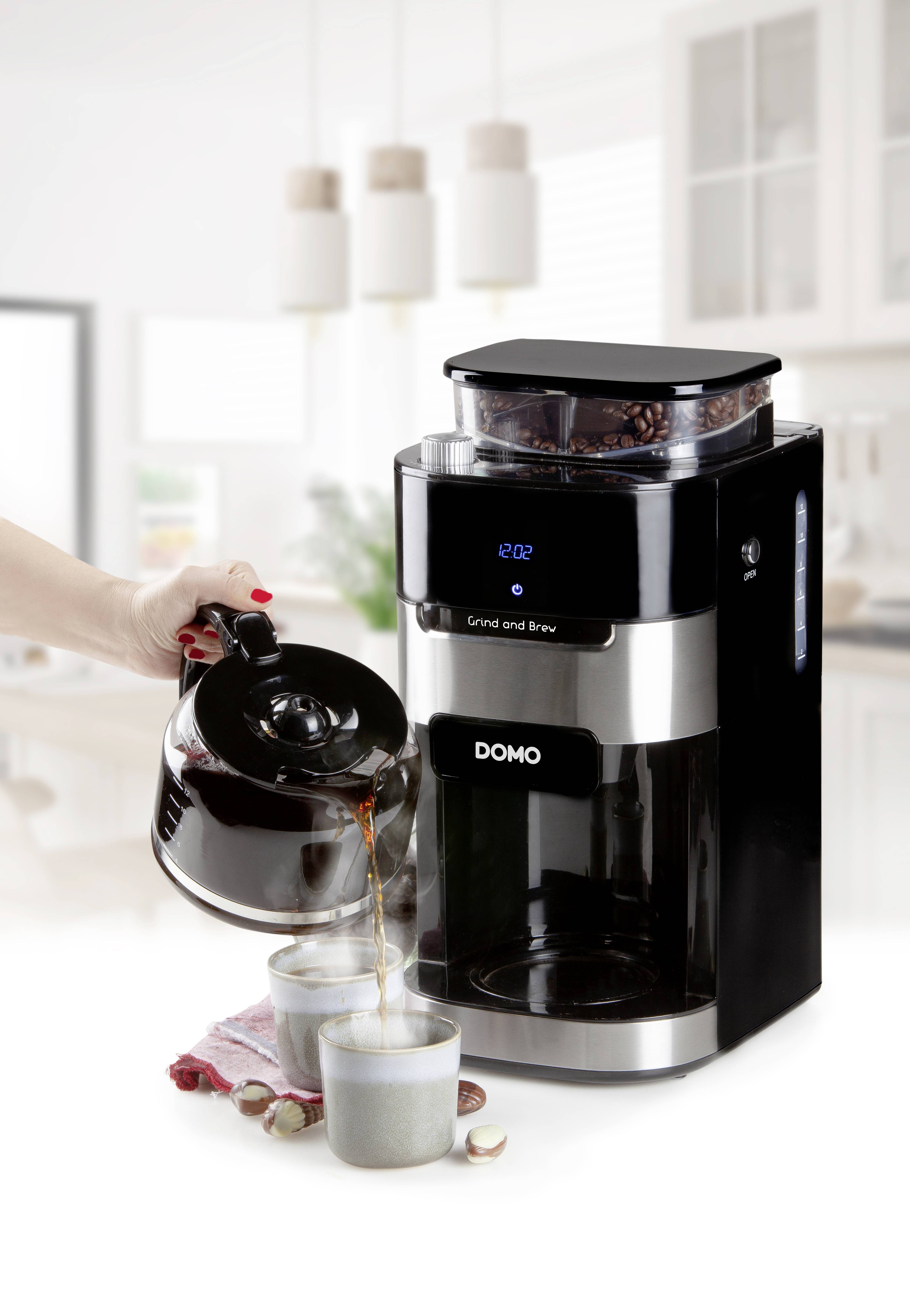 Eine Kaffeemaschine mit integriertem Mahlwerk; eine Hand gießt frisch gebrühten Kaffee in Tassen. Moderne helle Küchenumgebung.