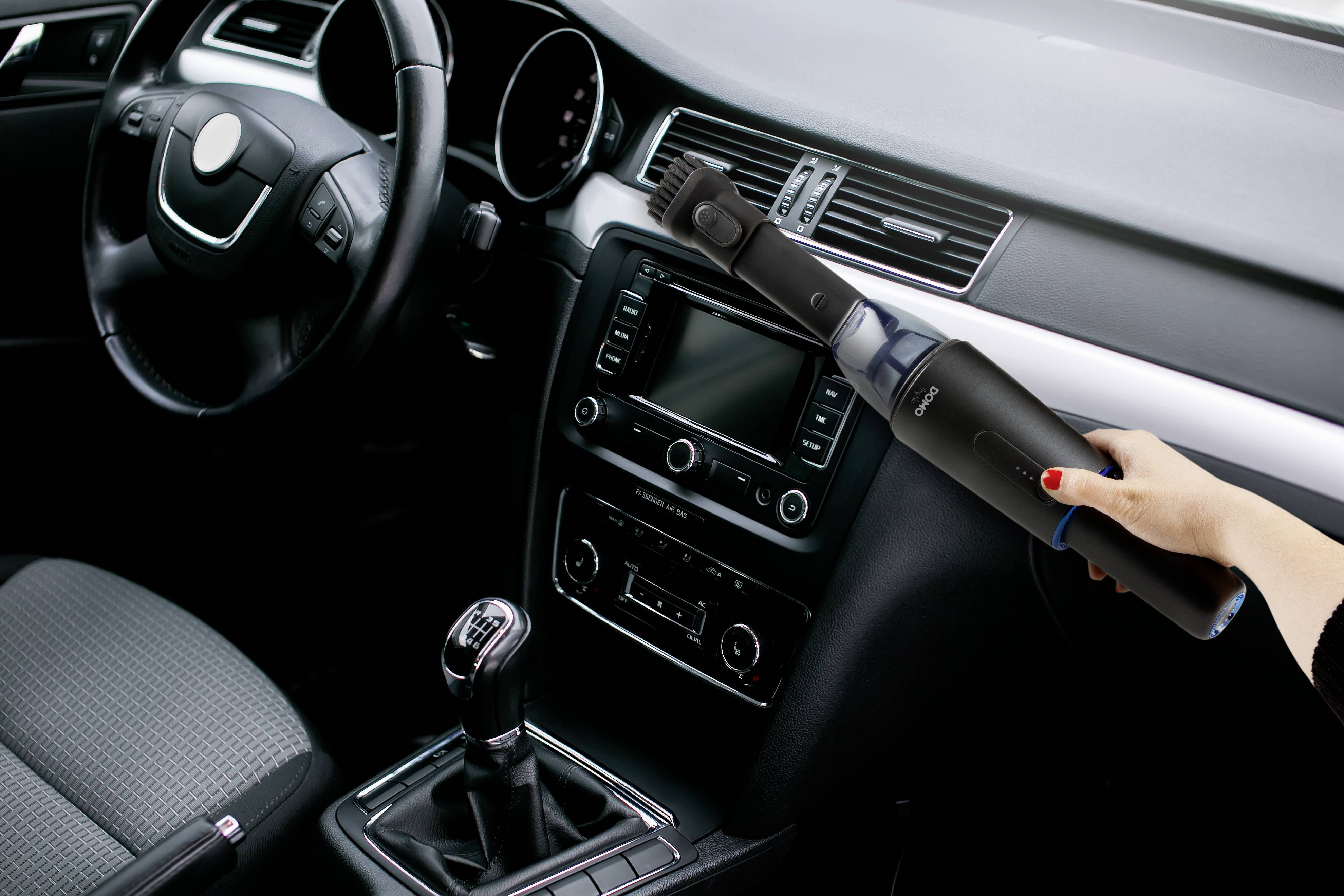 Eine Person benutzt einen kleinen, kabellosen Staubsauger, um den Innenraum eines Autos zu reinigen. Der Fokus liegt auf dem Gerät und seiner Anwendung.