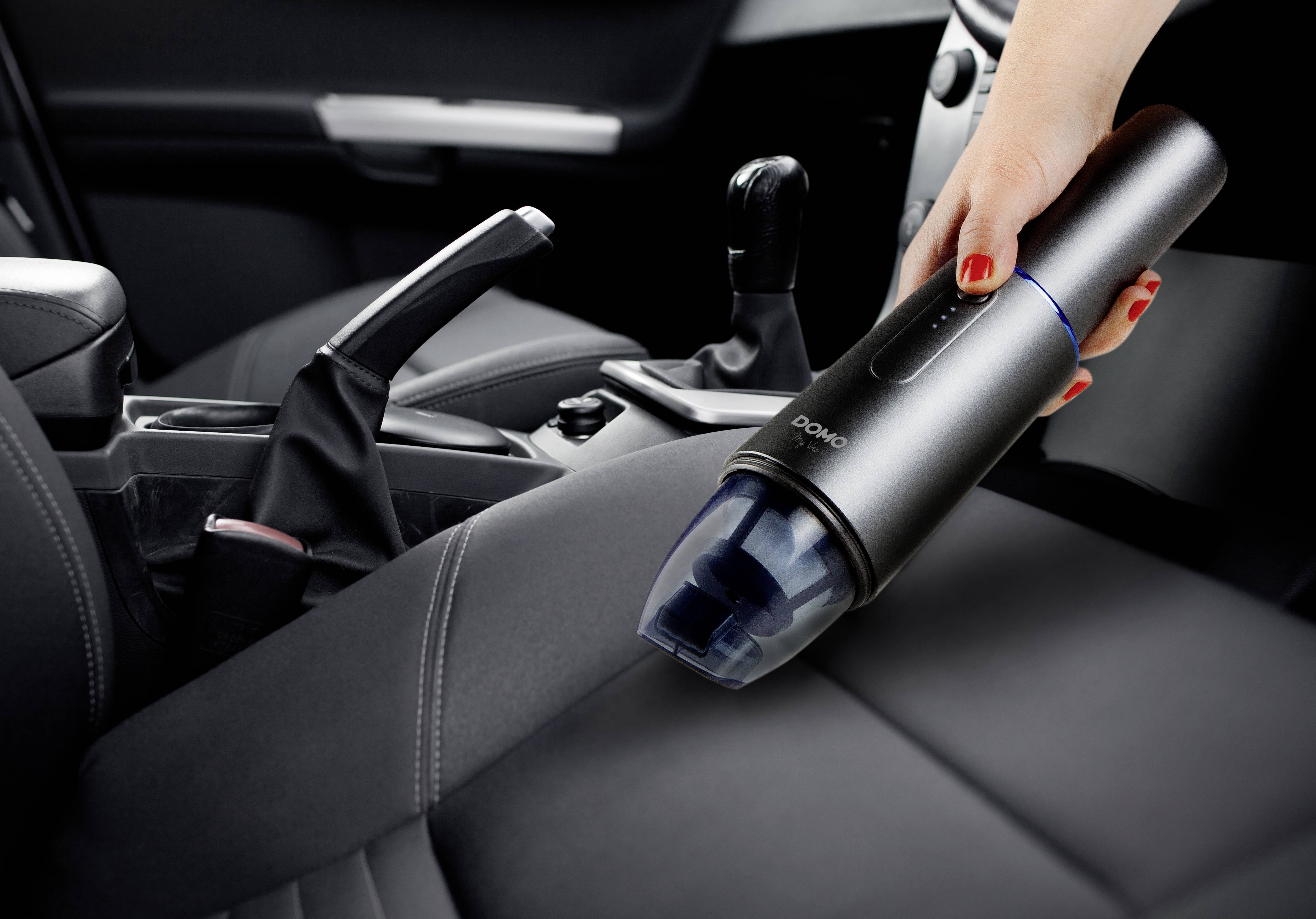 Hand reinigt Autositz mit tragbarem Staubsauger.