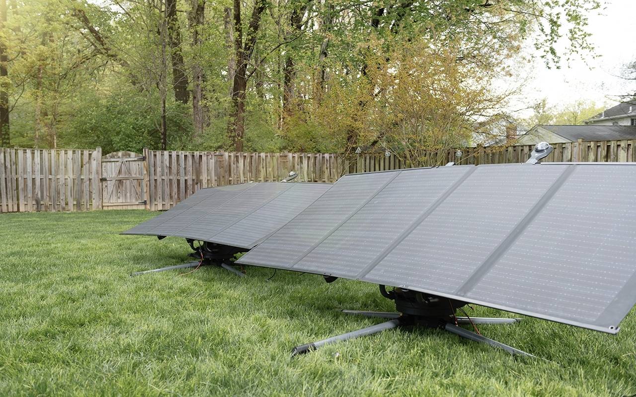 Drei Solarpaneele stehen auf einem Rasen in einem Garten, umgeben von einem Holzzaun und Bäumen im Hintergrund.