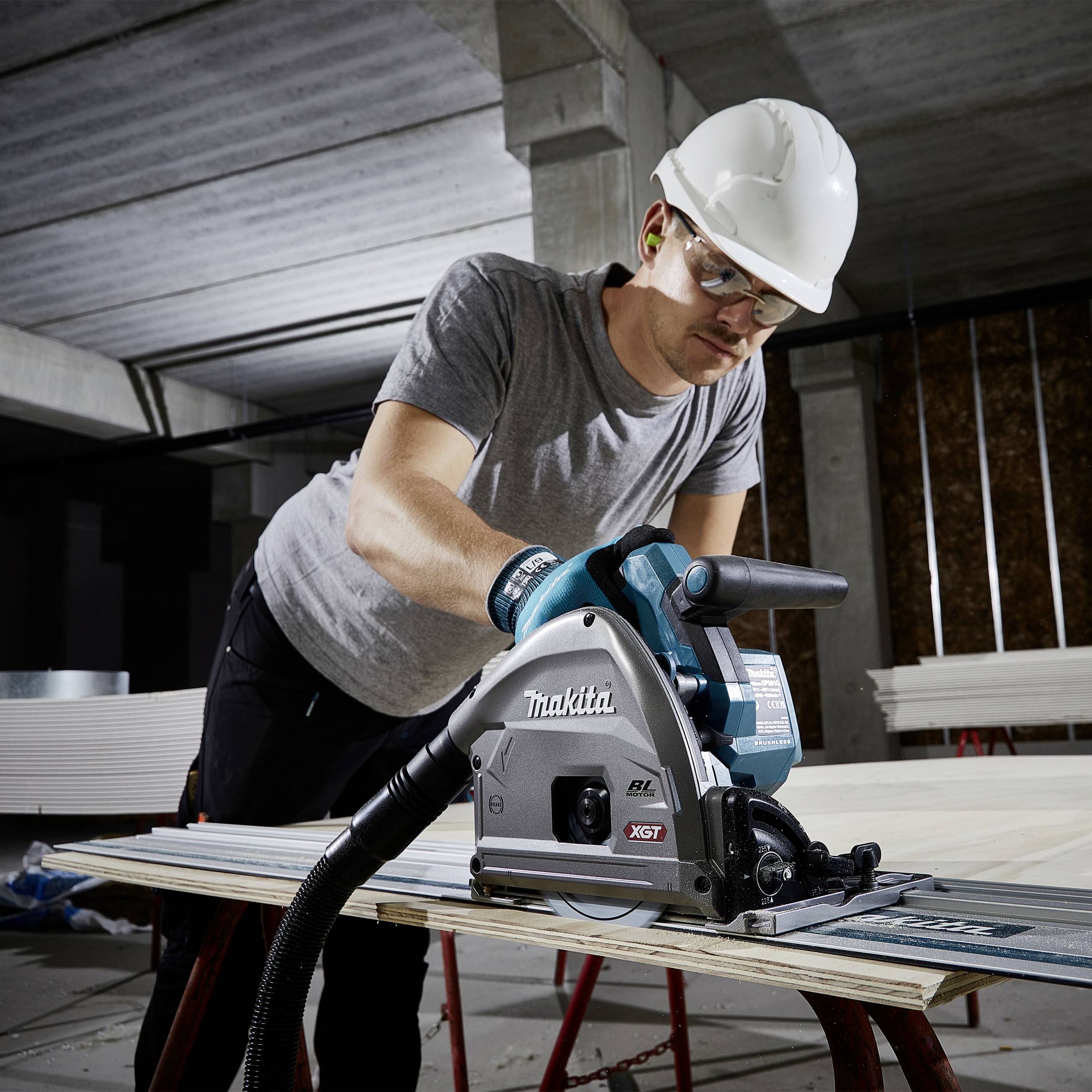 Ein Bauarbeiter mit Schutzhelm und Gehörschutz nutzt eine Handkreissäge, um Holz im Innenbereich eines Gebäudes zu schneiden.