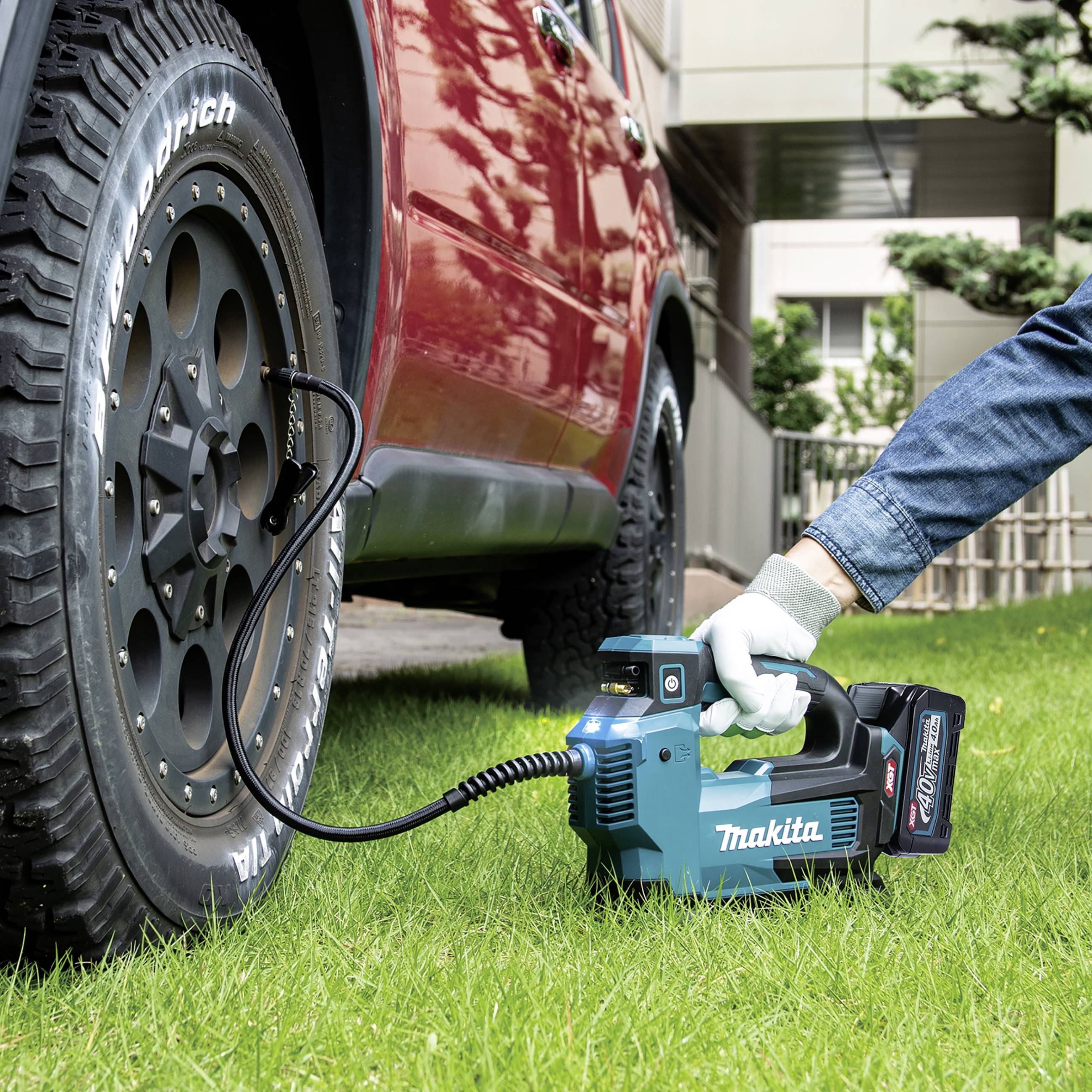 Ein Auto wird mit einem elektrischen Reifenfüller auf einer grünen Rasenfläche aufgepumpt. Eine Hand hält das Gerät.