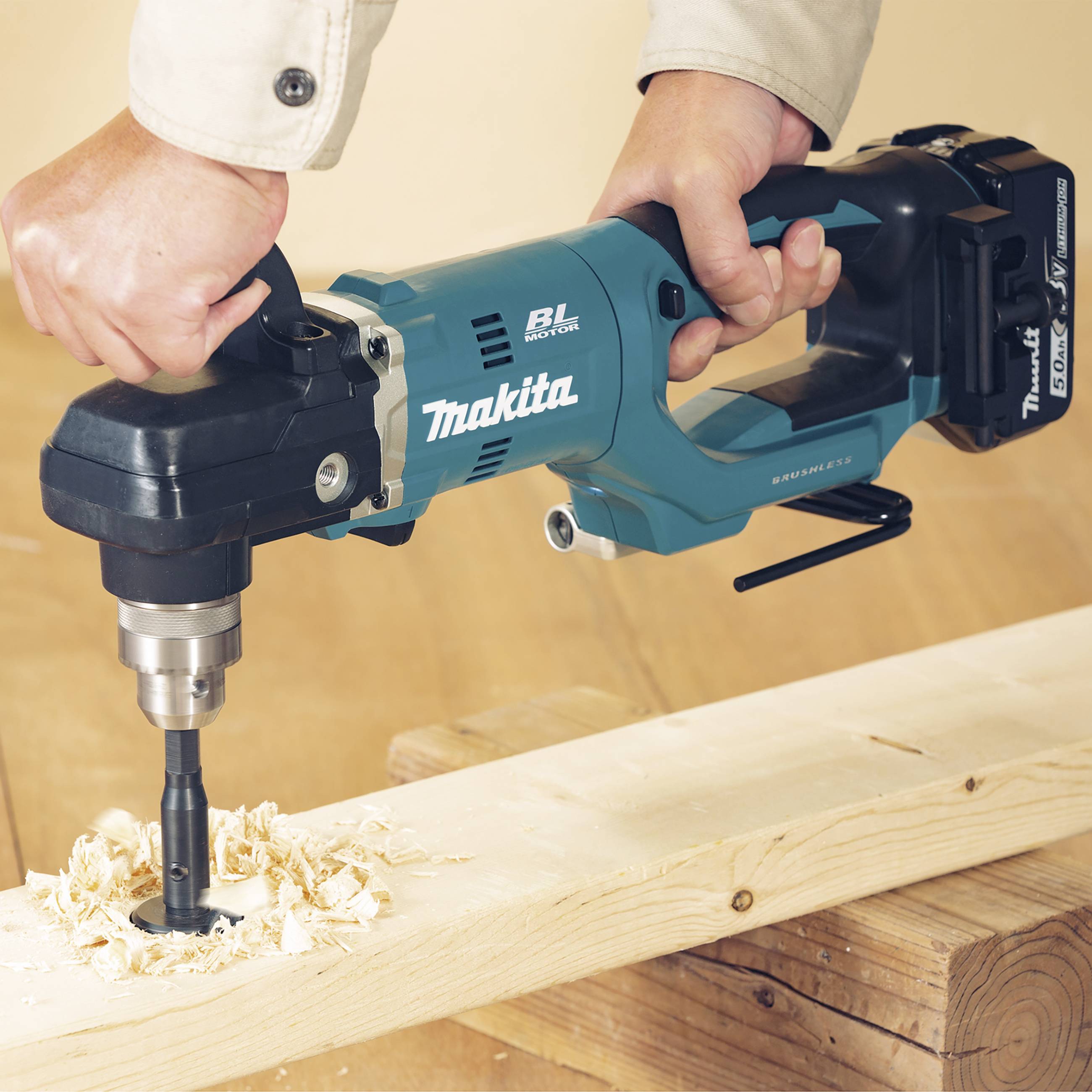 Eine Person bohrt ein Loch in ein Holzstück mit einer kabellosen Akku-Bohrmaschine. Holzspäne um das Loch herum sind sichtbar.