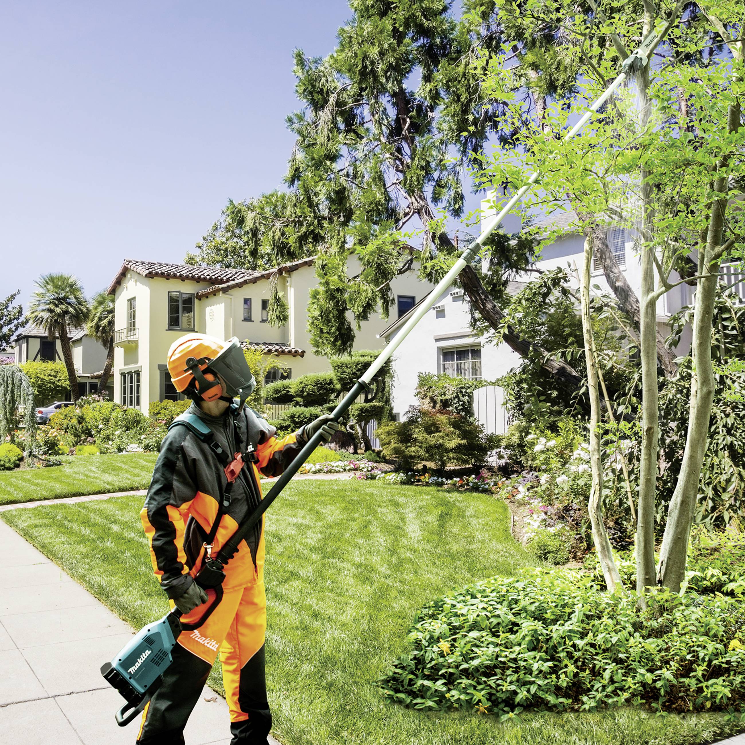 Eine Person in Schutzkleidung schneidet mit einer elektrischen Heckenschere Äste von einem Baum in einem gepflegten Garten.